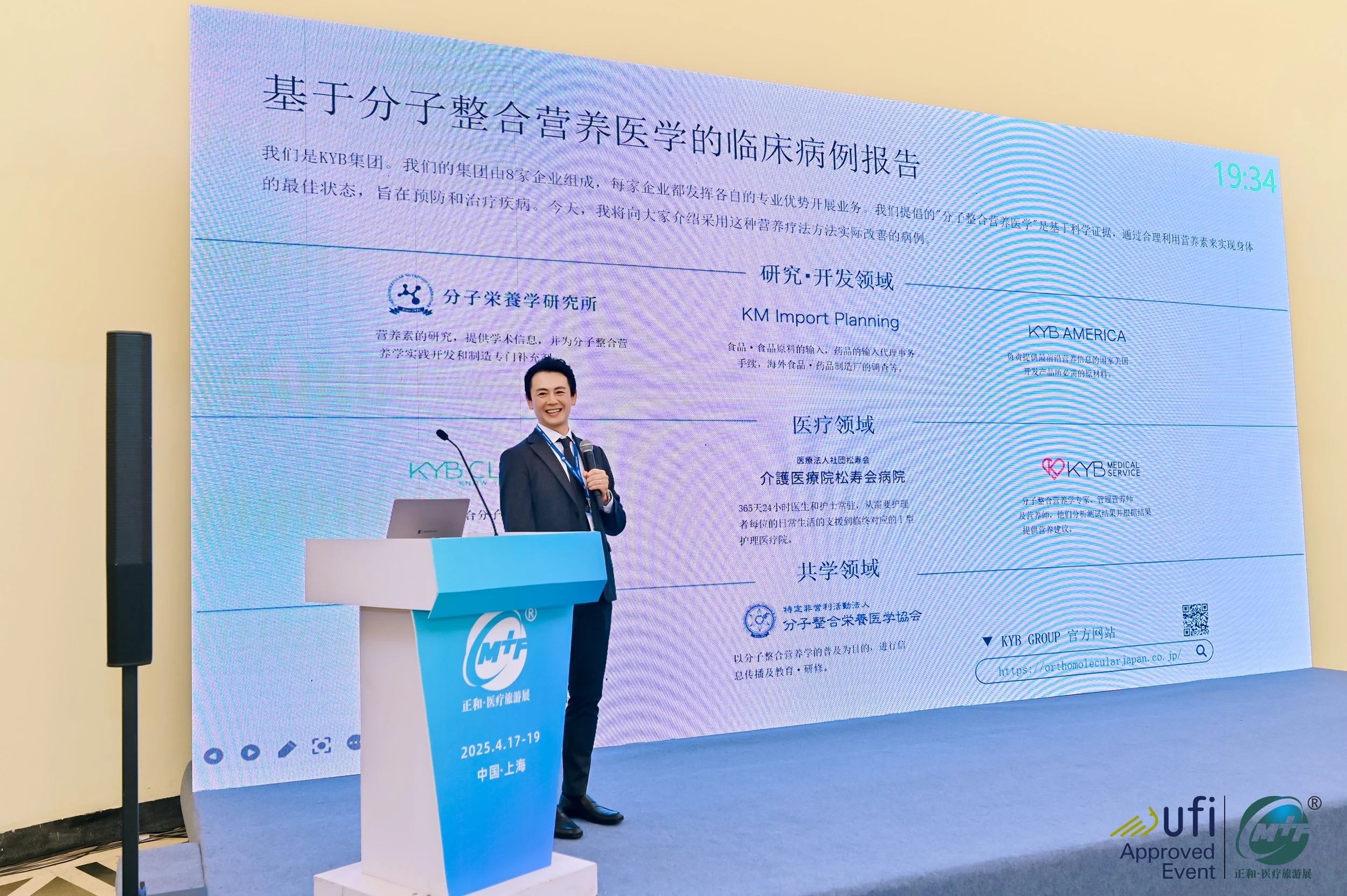 A woman in a dark suit and tie stands on a stage, smiling and holding a microphone, in front of a large screen displaying Chinese text about a clinical case report related to nutrition and medical studies, with event details including the date '2025.4.17-19' and location 'Shanghai'.