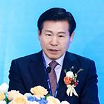 A man in a suit speaking at a formal event with a blue background.