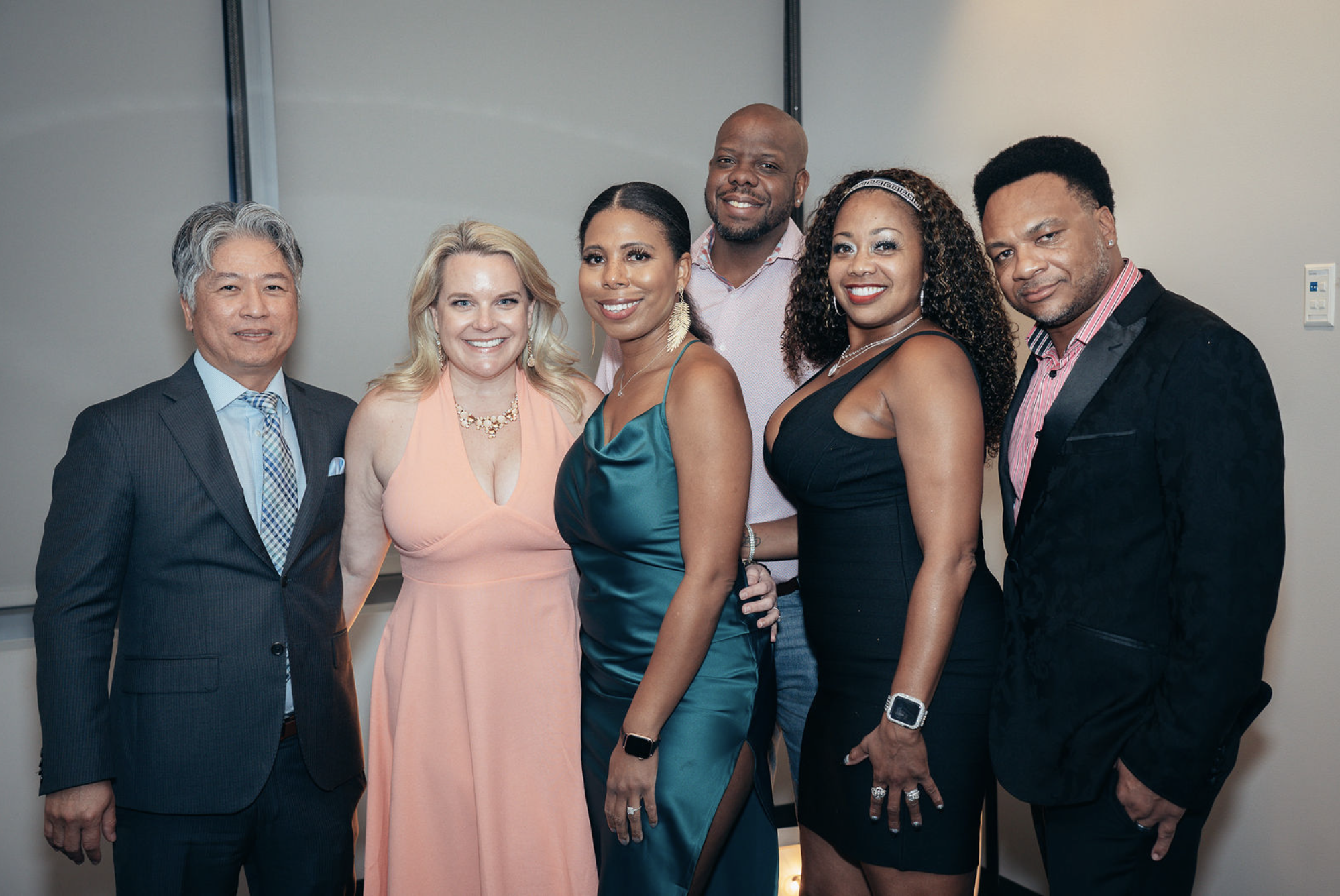 Group of six diverse people dressed in formal attire posing for a photo in a conference room or event space.
