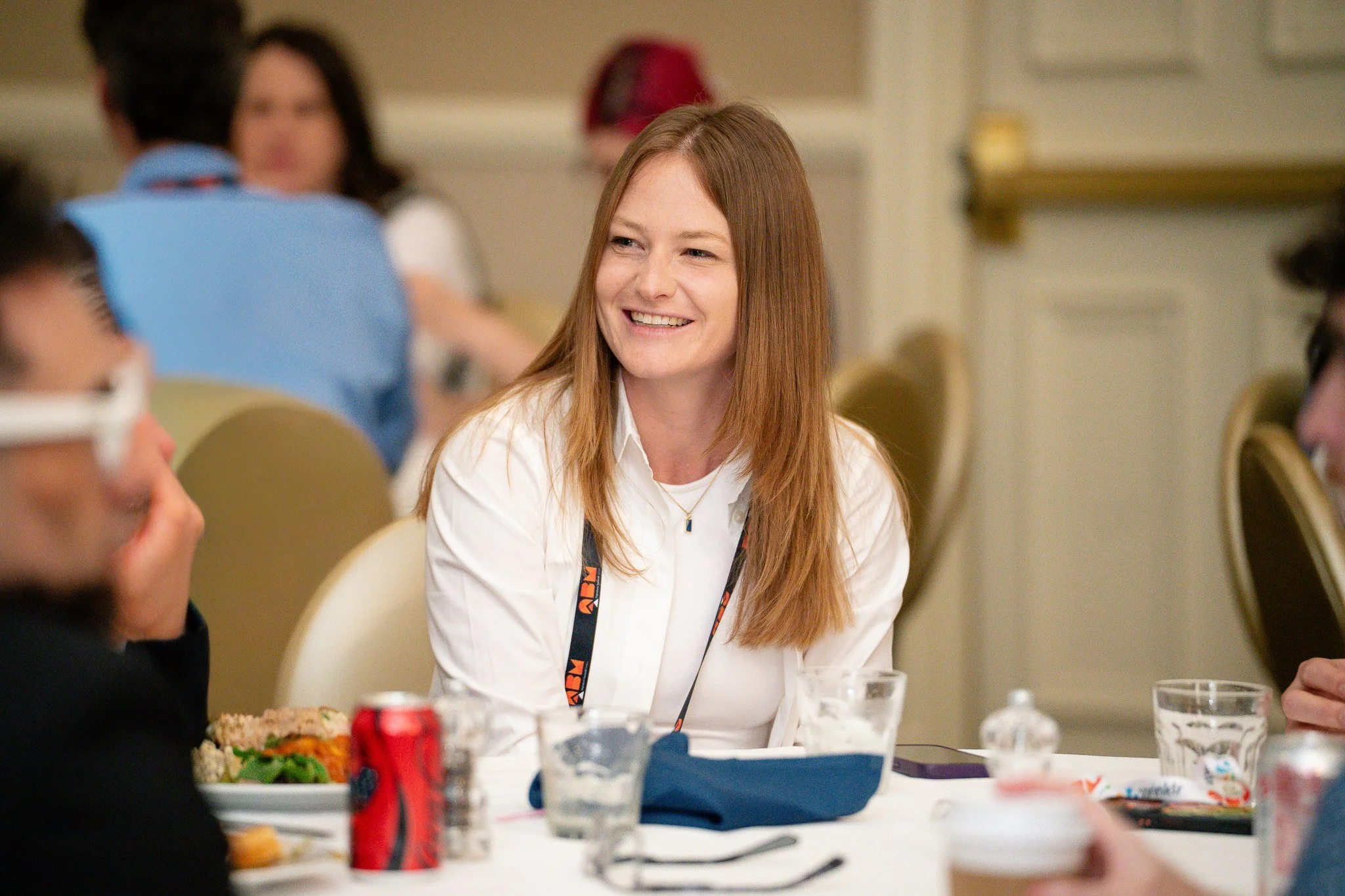 A woman with long red hair is smiling and talking with a group of people at a table during a social gathering or meeting.