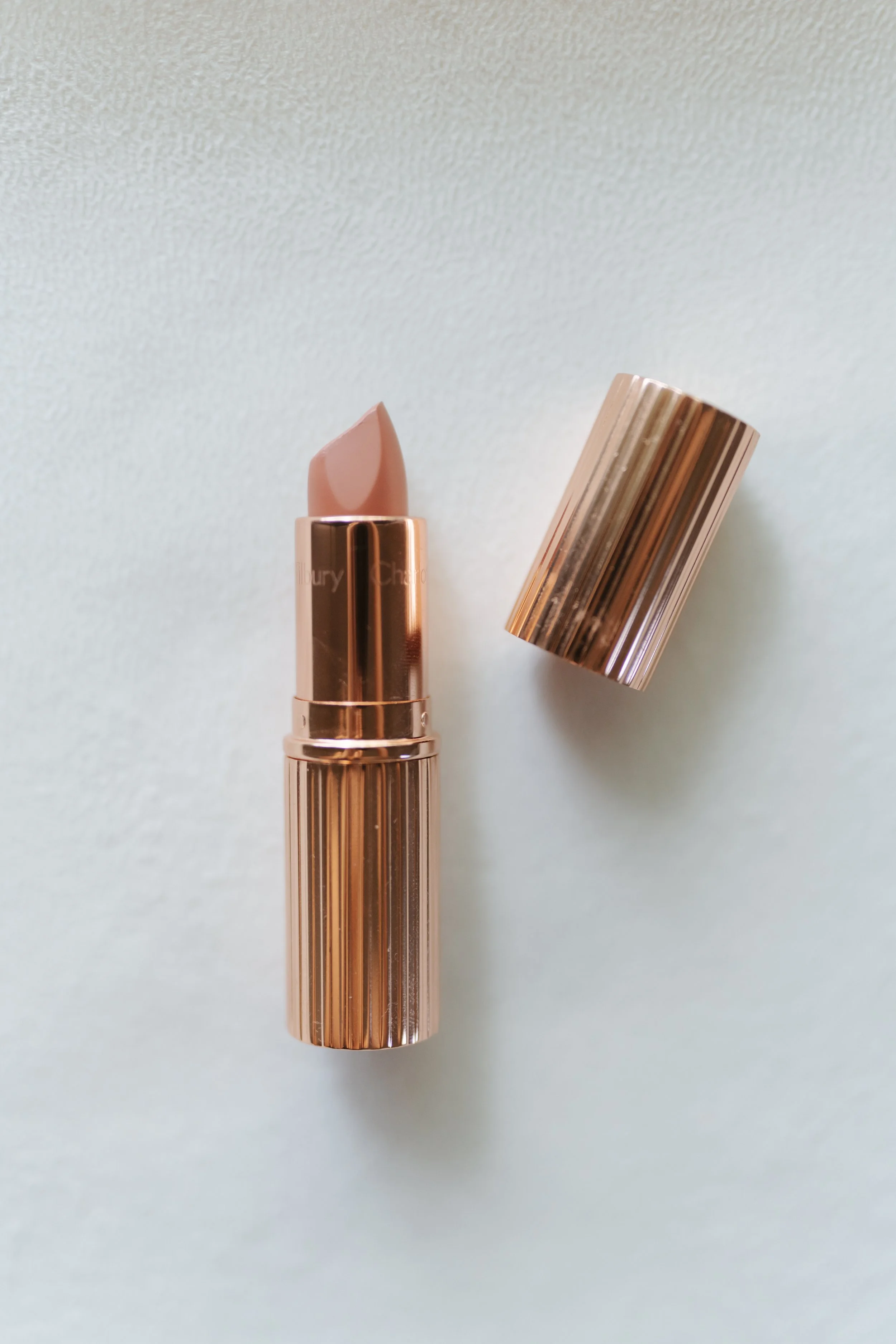 A tube of nude lipstick with a rose gold metallic case and its cap placed beside it.