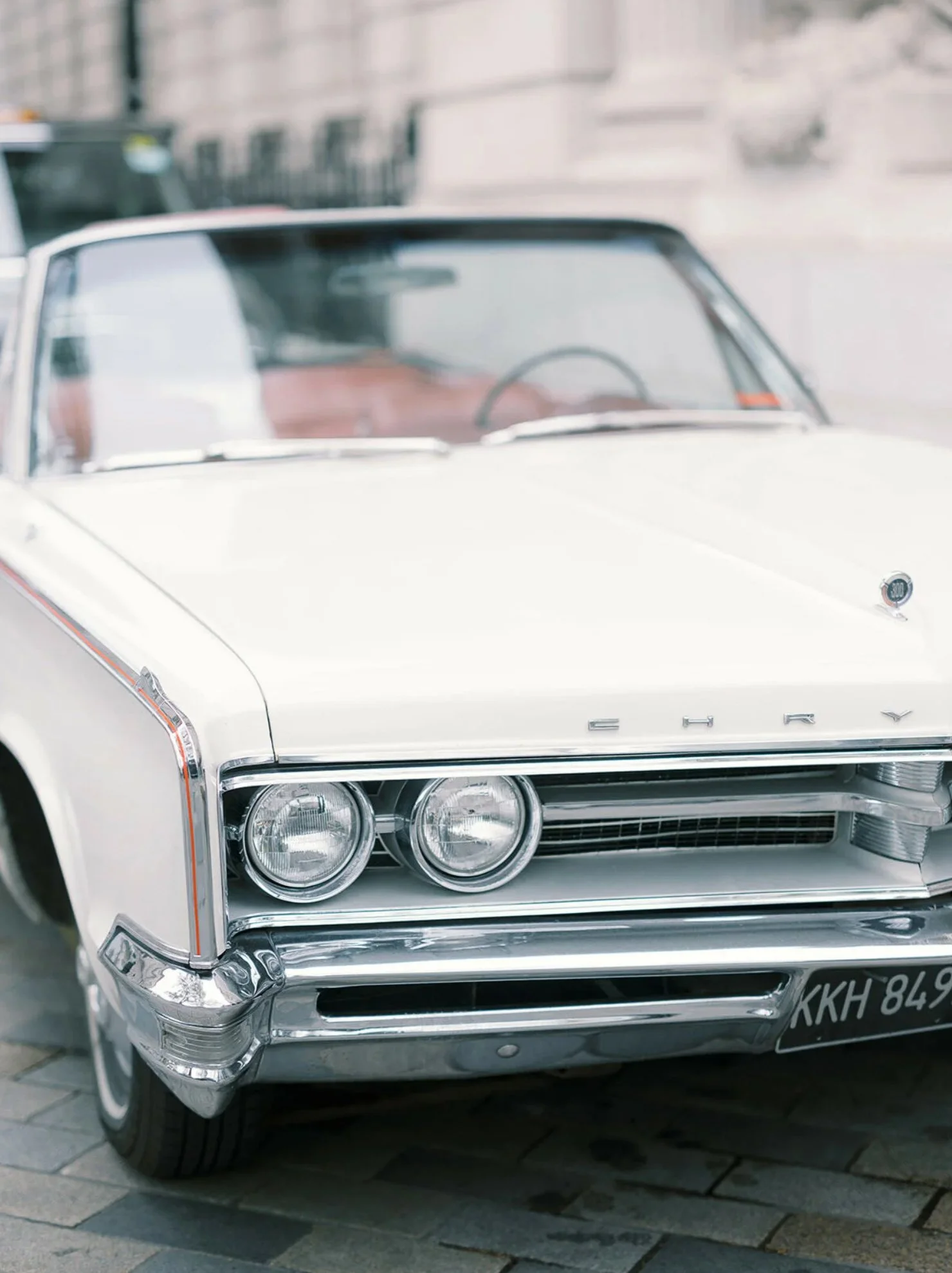 front view of a vintage white Chrysler car from the 1960s parked on a city street.
