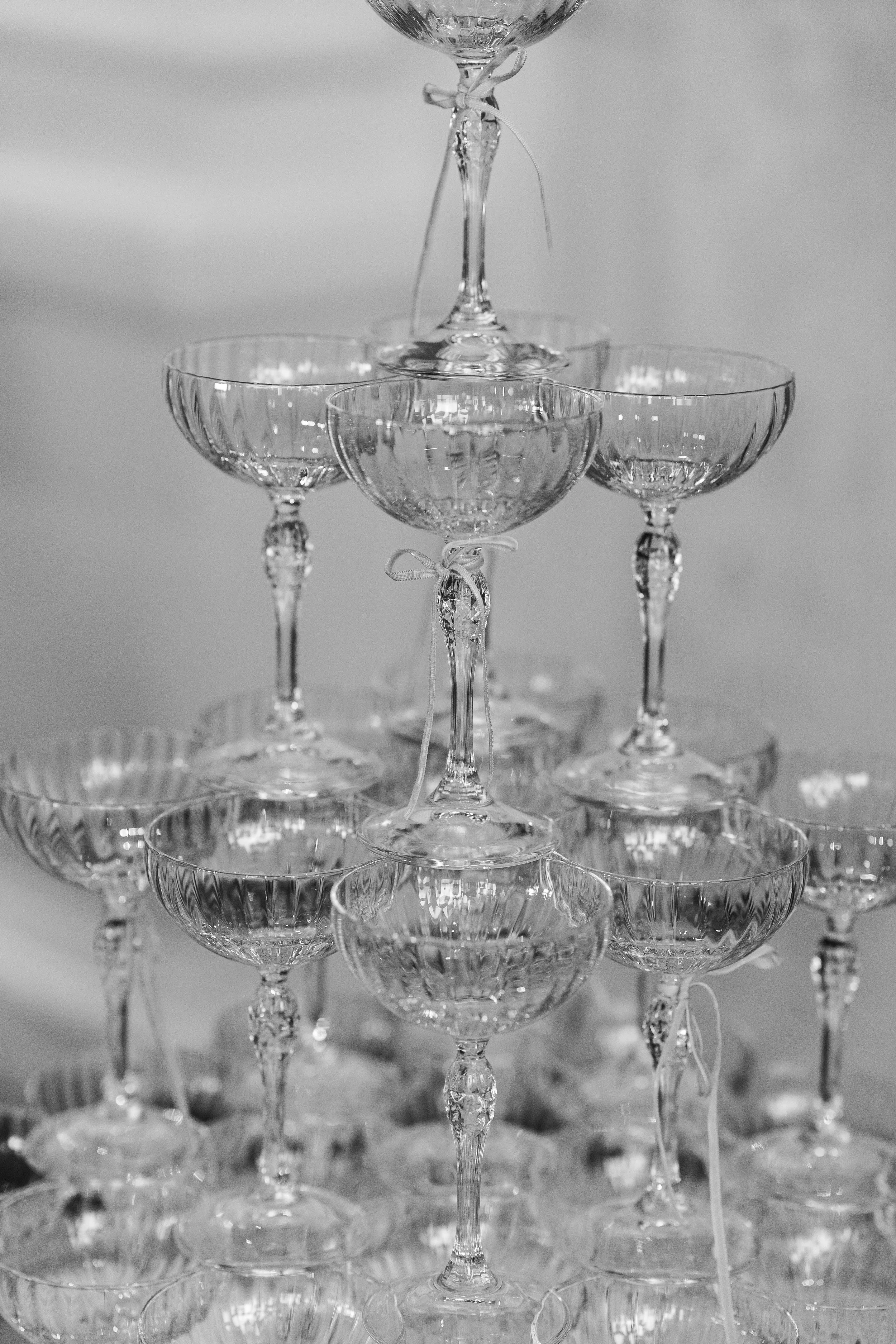 Stacked champagne glasses with ribbons tied on some of the stems, in black and white.