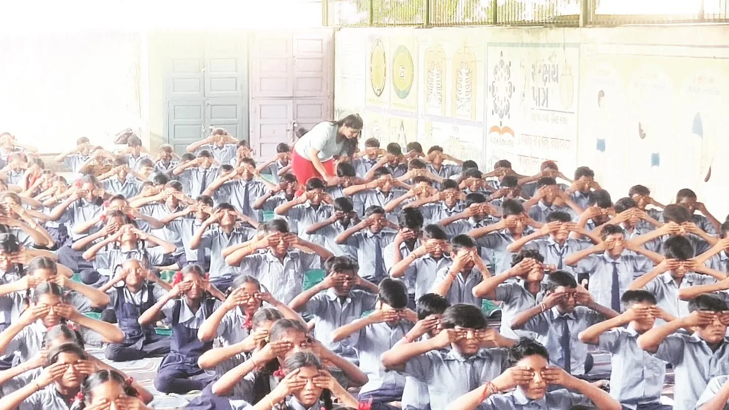 A large classroom full of students in school uniforms doing eye exercises, with a teacher supervising.