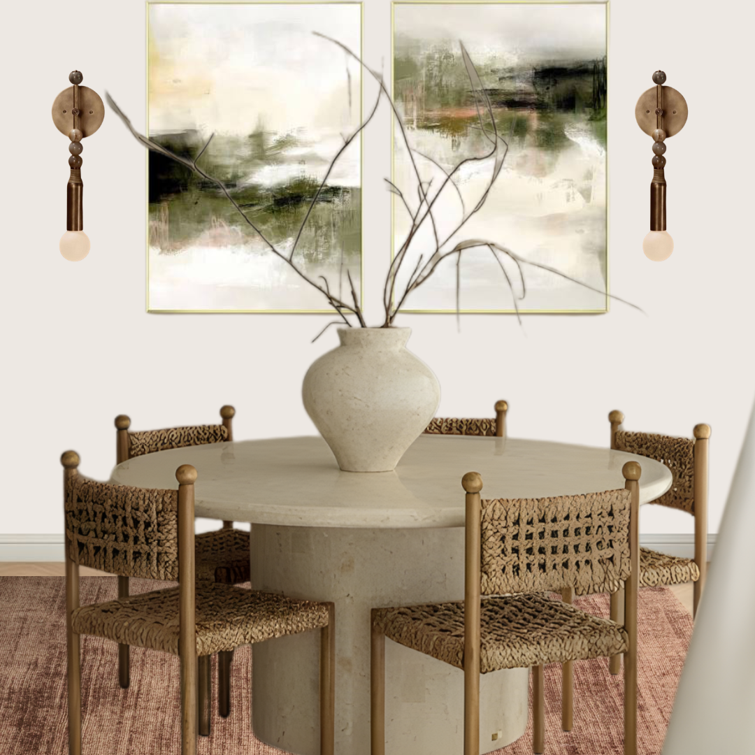 A round dining table with a large ceramic vase containing bare branches in the center. Four chairs with woven seats surround the table. Two abstract landscape paintings are hung on the wall behind the table, with wall-mounted light fixtures on either side of the paintings.
