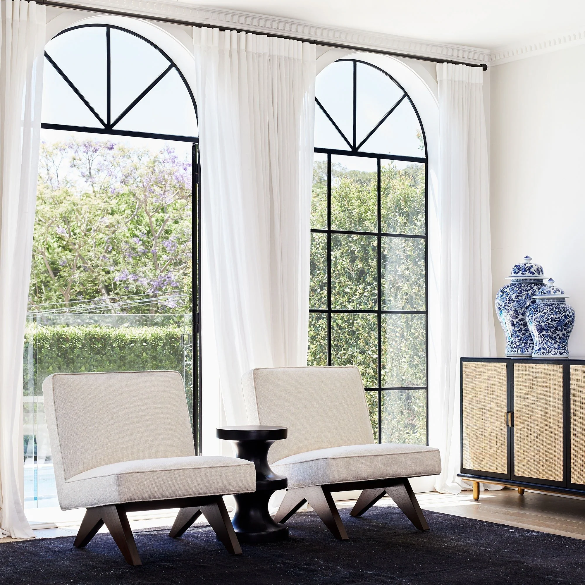 Coco Republic accent chairs styled in bright living room with arched windows and soft neutral palette.