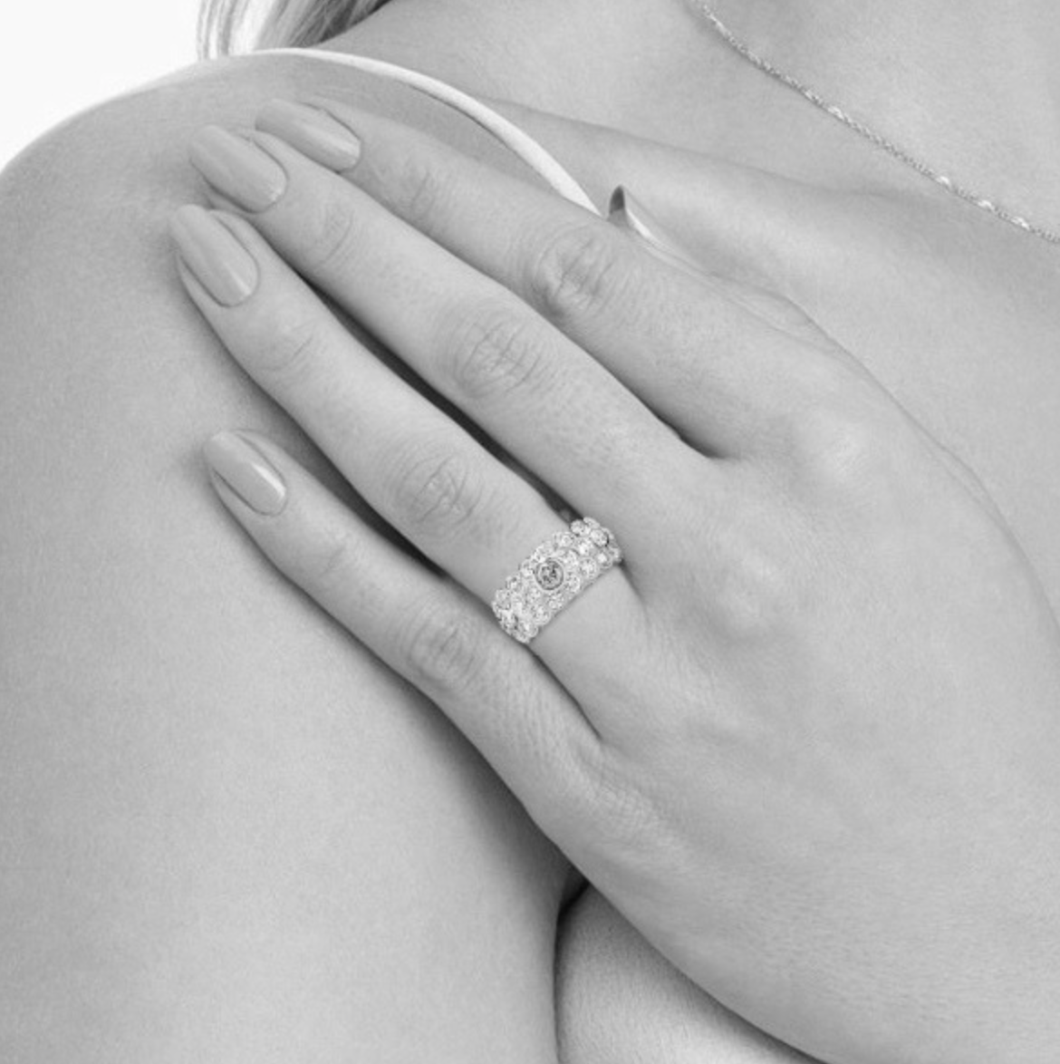 Close-up of a woman's hand wearing an engagement ring with multiple diamonds, resting on her shoulder.