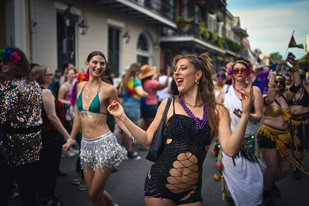 People celebrating at a parade during daytime, wearing colorful and festive costumes, dancing and enjoying the event on a city street.