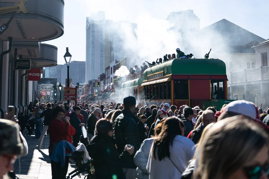 People crowd the street as a steam train passes through during a parade or festival in an urban area.
