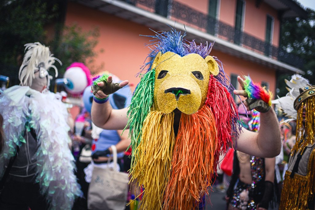 Person wearing a lion mask with a rainbow-colored fringed mane at a parade.