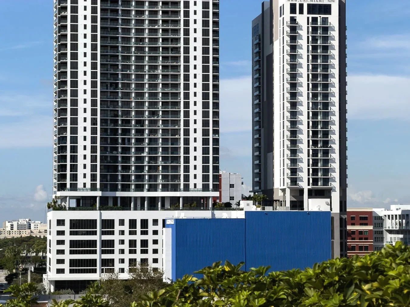 Two high-rise buildings under a partly cloudy sky, with trees and smaller buildings in the foreground by a experienced photographer. 