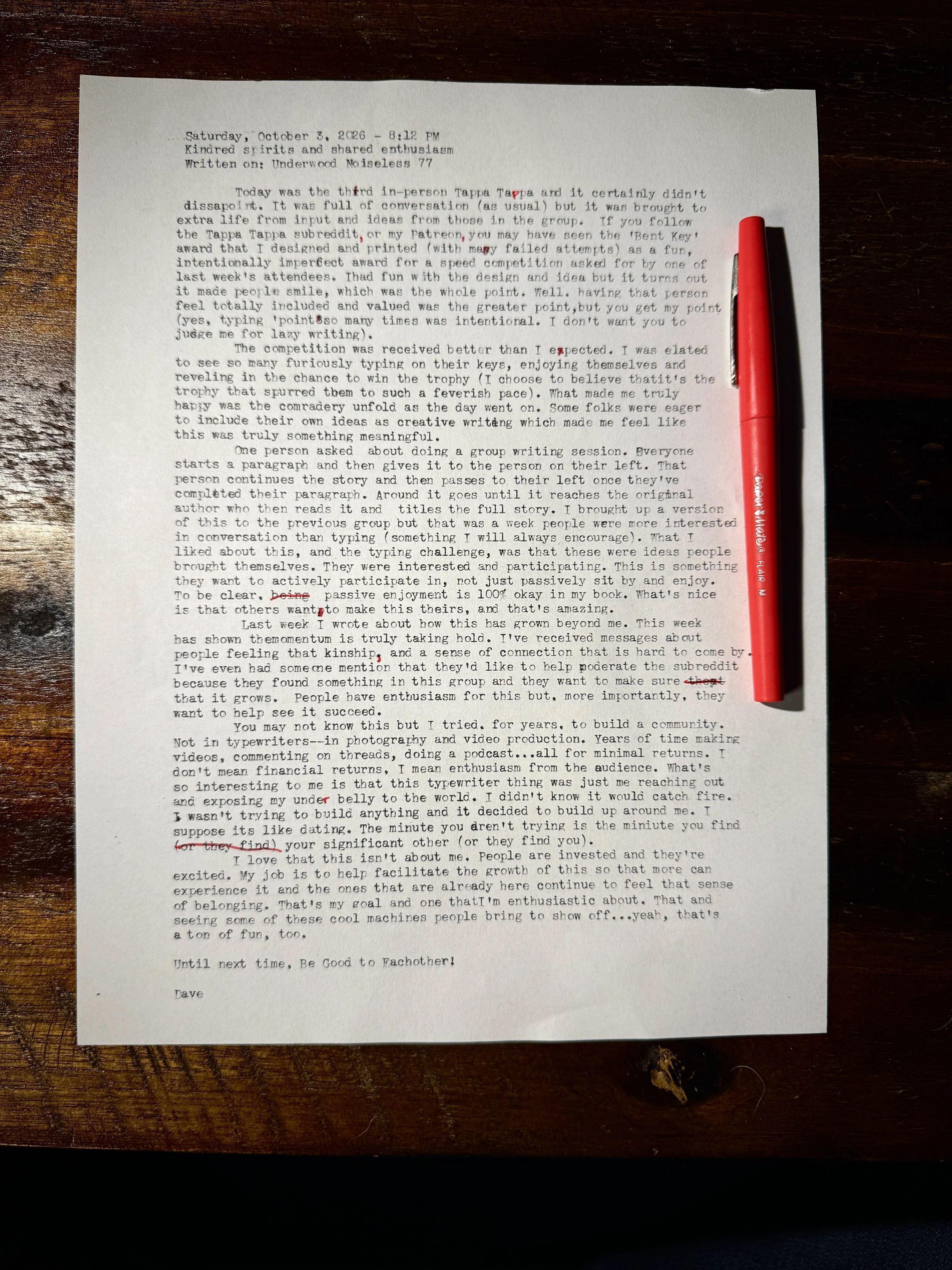 Typewritten Tappa Tappa meetup reflection with handwritten red corrections, photographed on a dark wooden table beside a red pen.