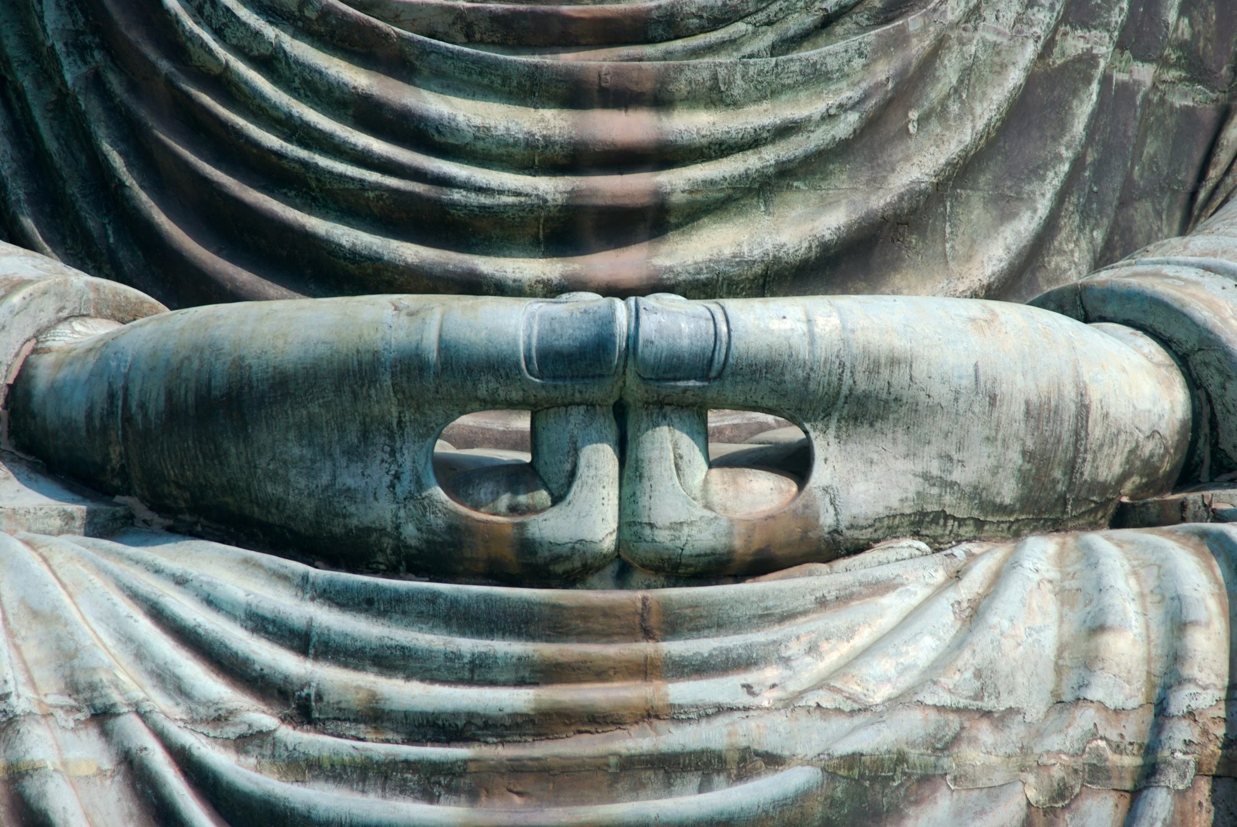 Close-up of the Buddha statue's chest and peaceful hands in a meditative pose, showing detailed folds in the robes and a serene expression.