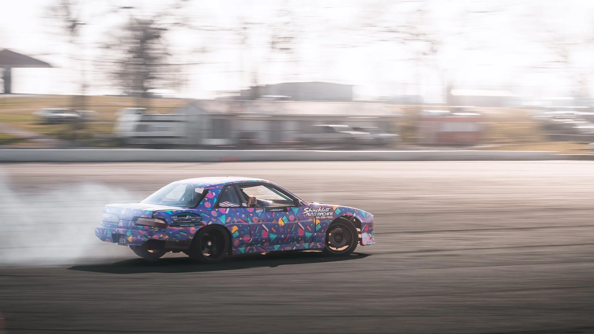 A colorful race car with abstract patterns drifting on a race track, producing smoke from the rear tires.