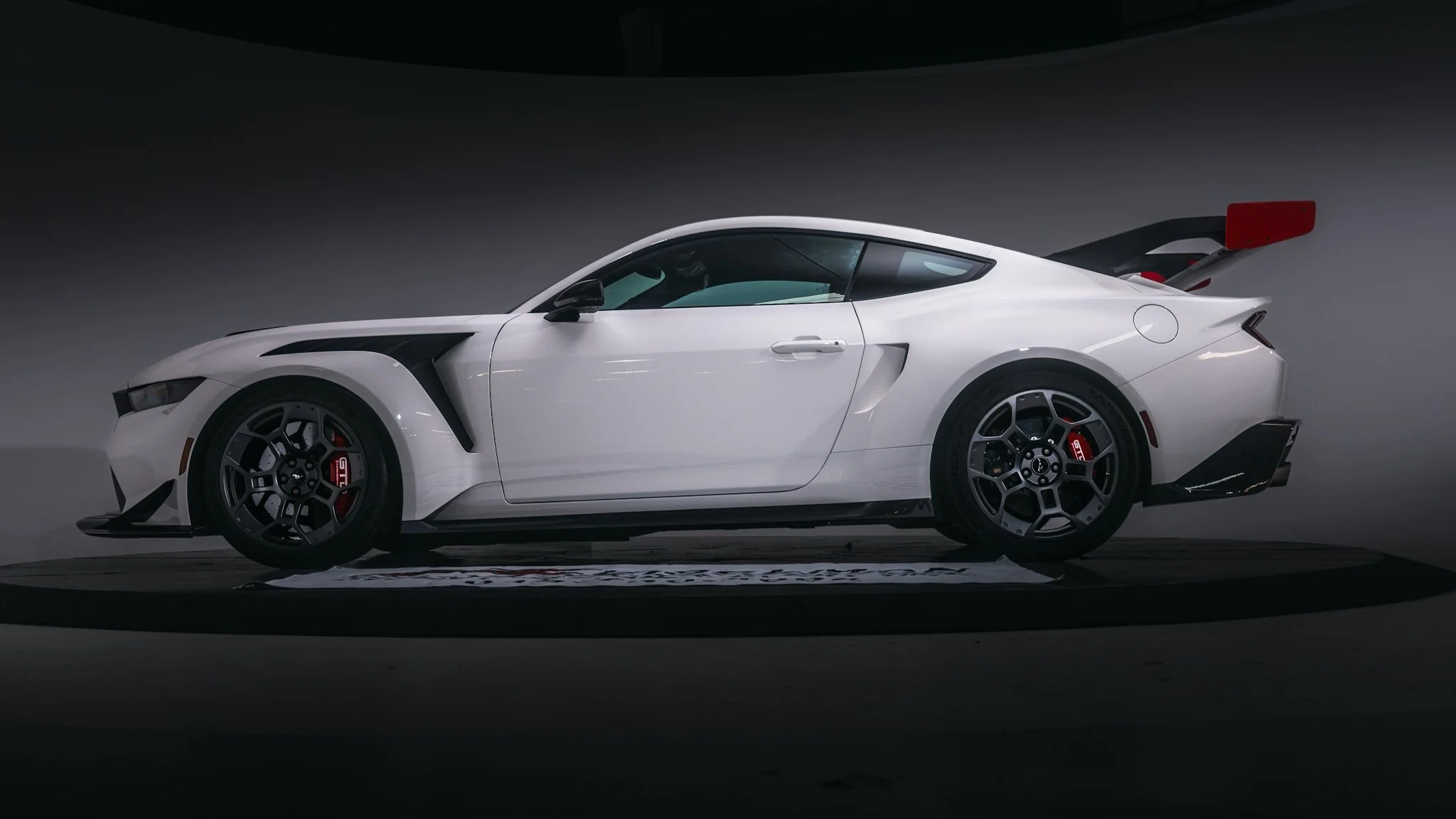 Side view of a white sports car with black and red accents, large rear wing, and racing wheels.