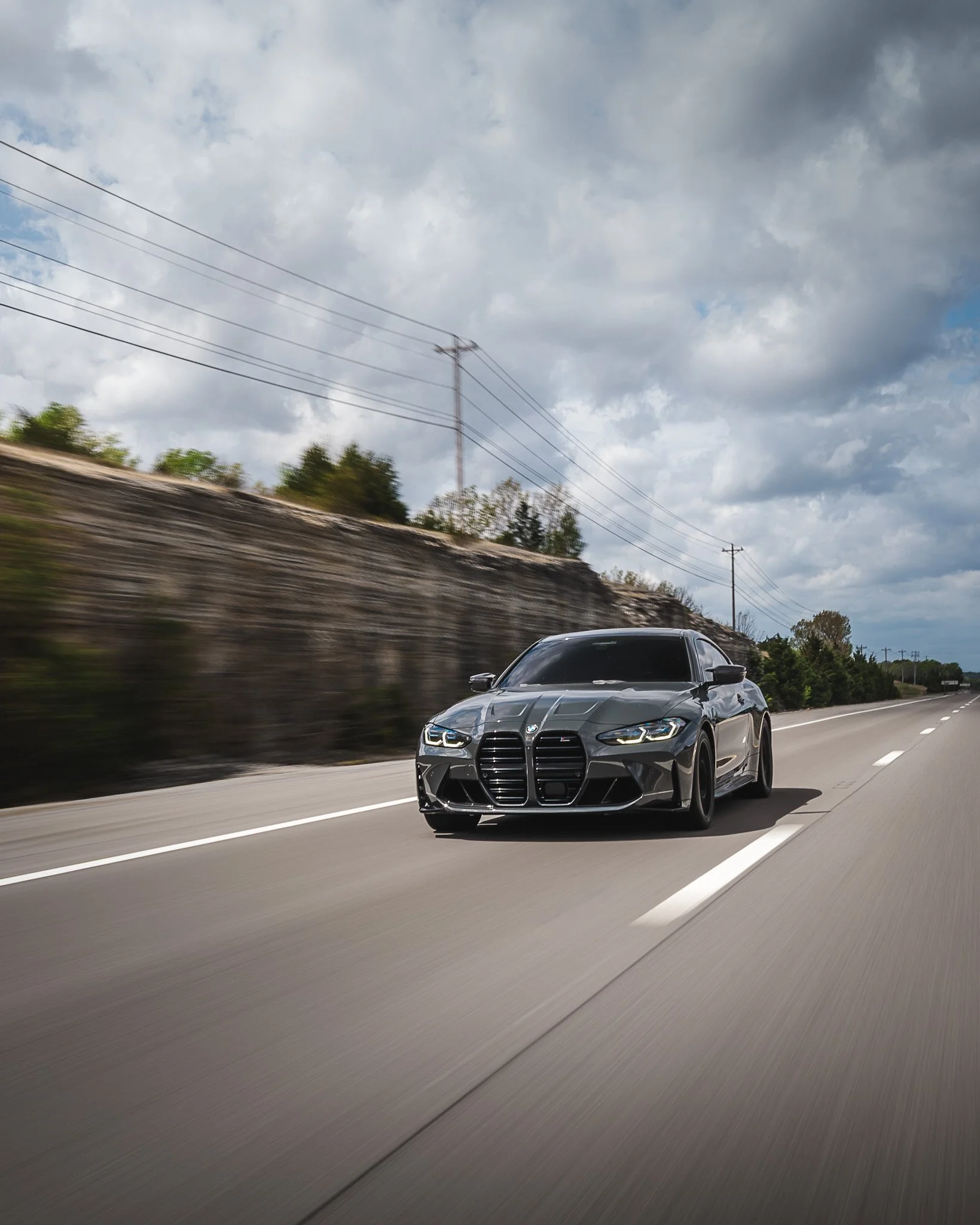 A sleek, black sports car driving on an open highway with a cloudy sky overhead.