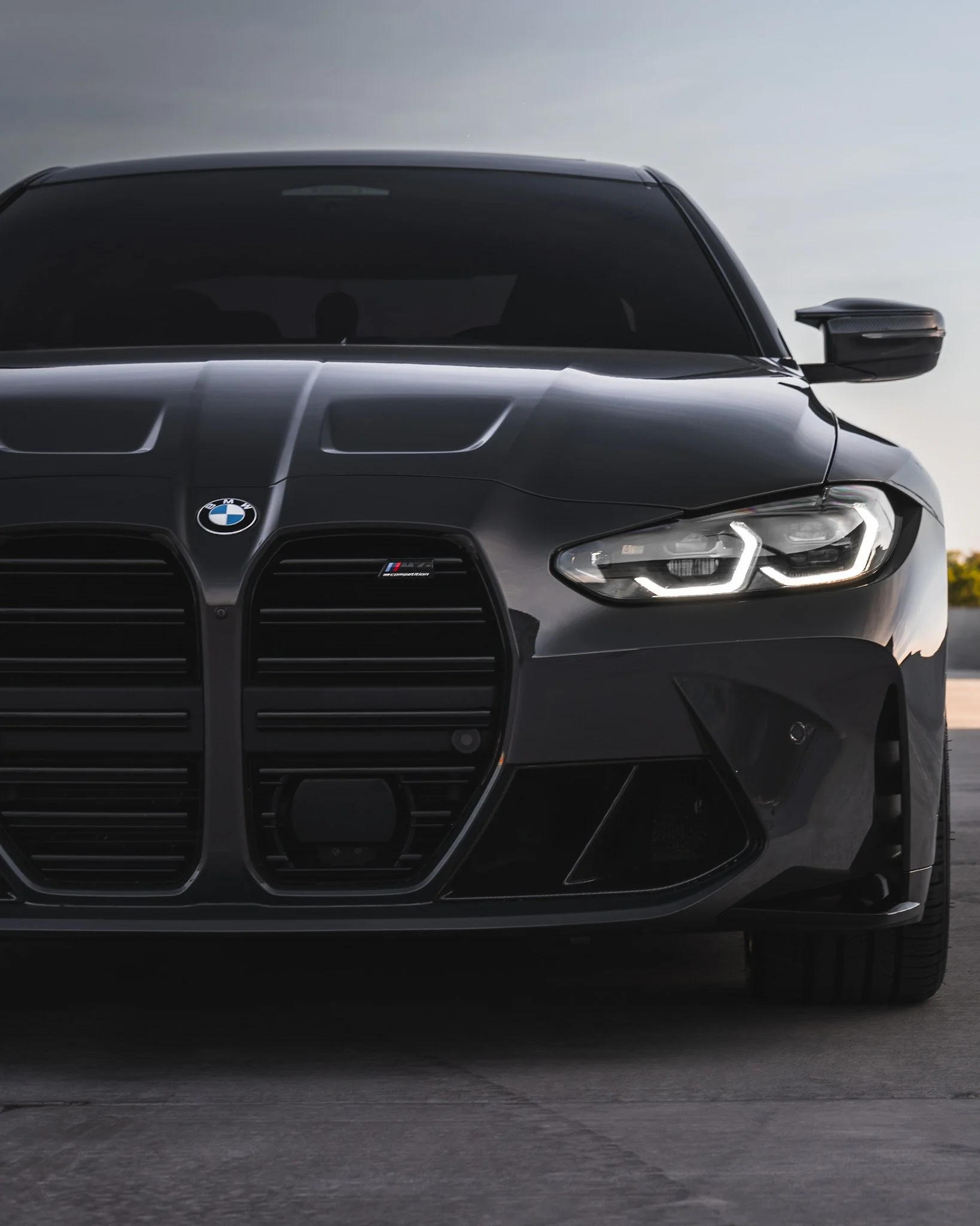 Front view of a black BMW luxury car parked on a paved surface, with a visible BMW logo and modern LED headlights, during dusk.