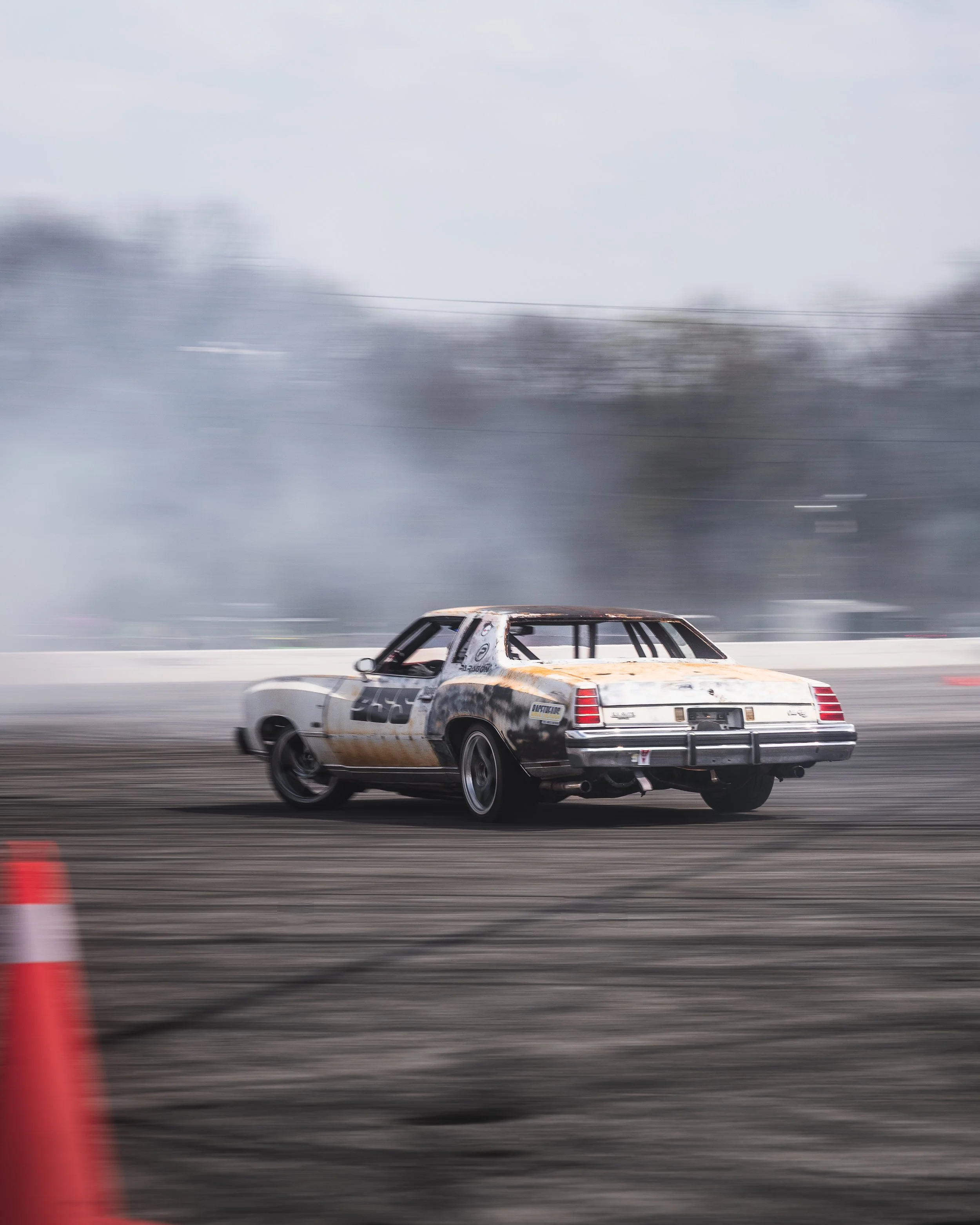 A race car speeding on a track, with smoke and motion blur effects, and orange cones in the foreground.