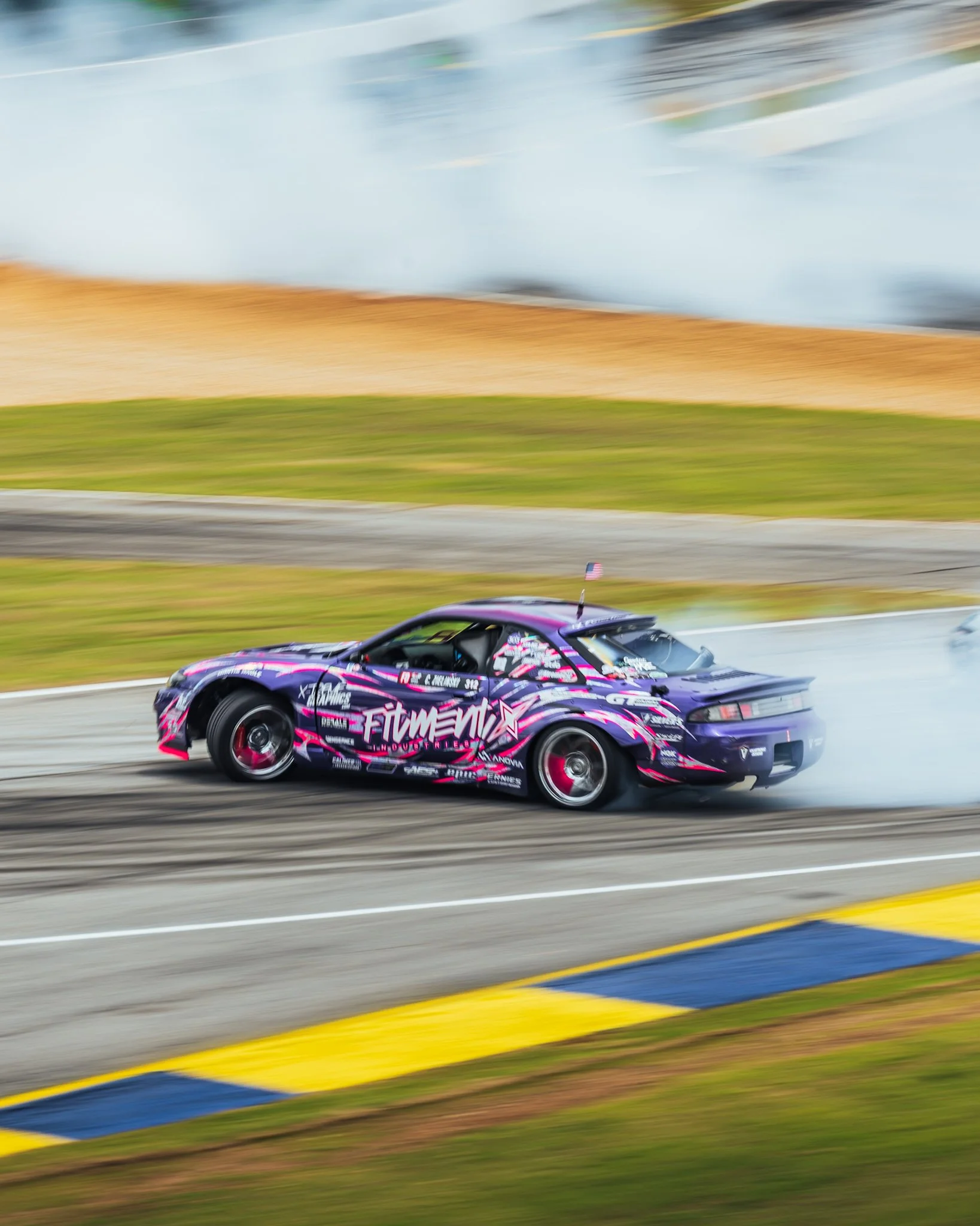 A racing car with purple, pink, and white graphics speeding down a track, creating a motion blur effect.