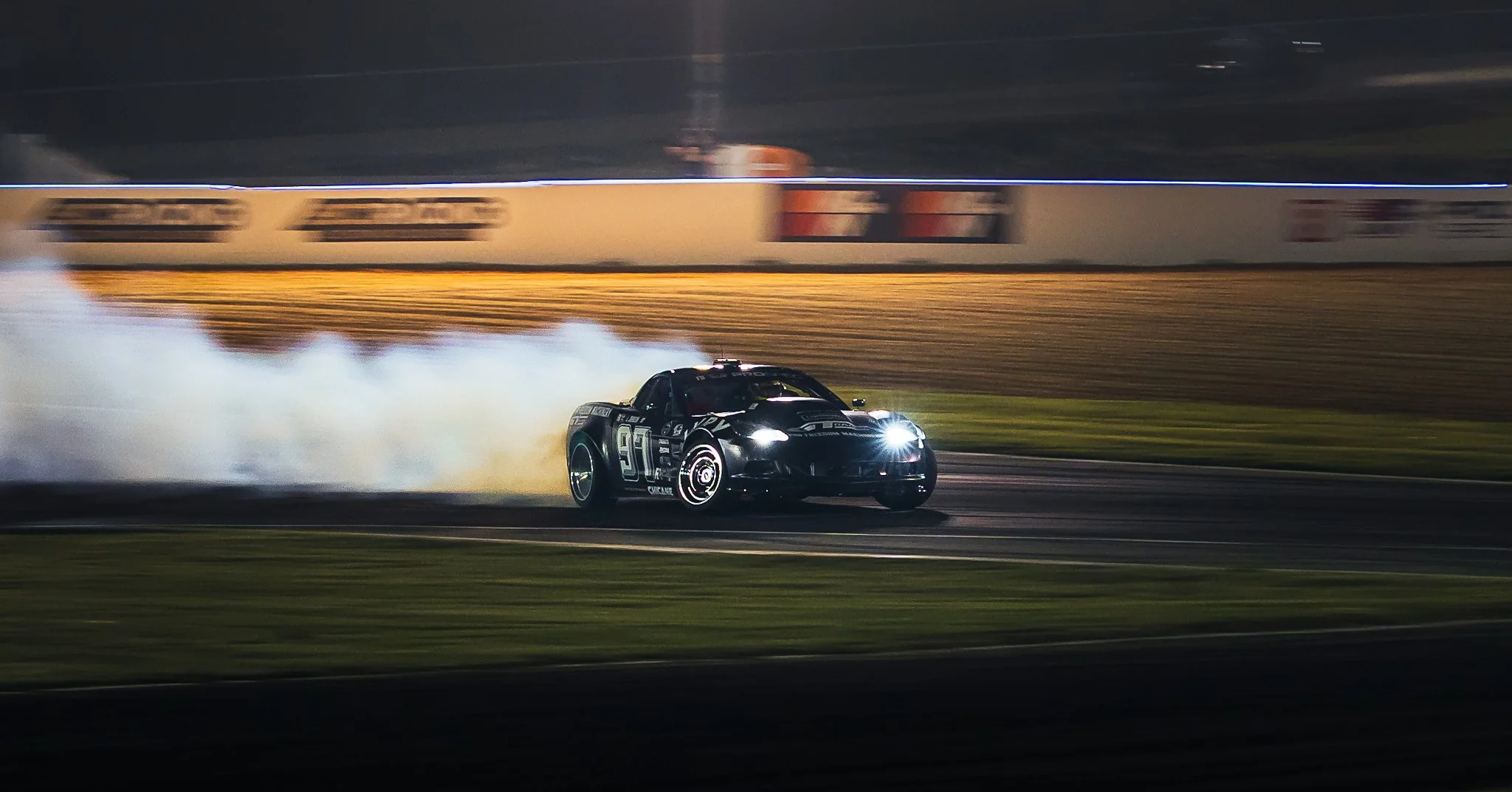 A black race car speeding on a track at night, kicking up smoke from its tires.