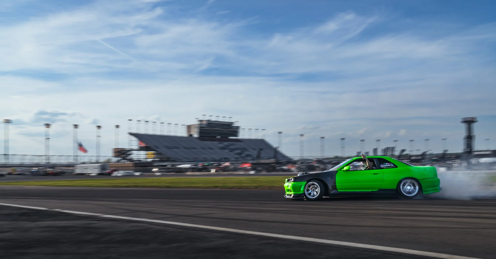 A green and black nissan skyline drifting on at Nashville Superspeedway with clouds and racing stands in the background.