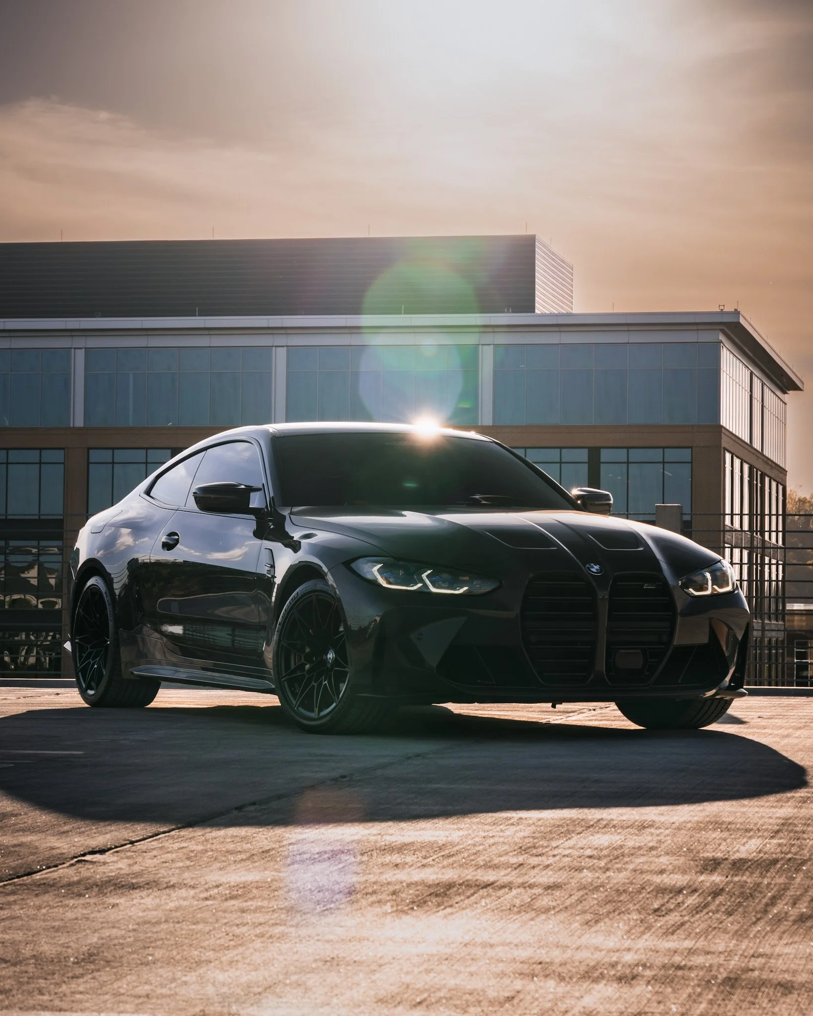 A black BMW car parked in an outdoor parking lot during sunset with a modern building in the background.