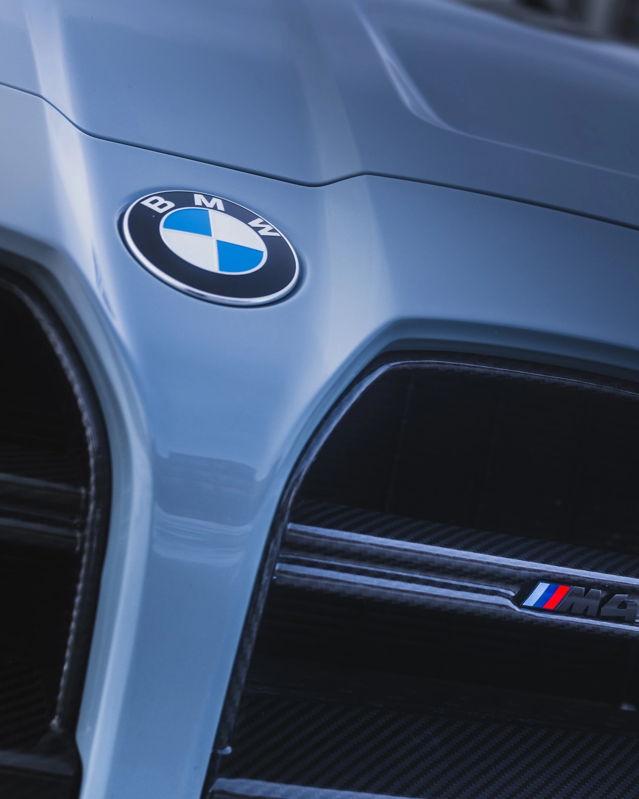 Close-up of the front part of a BMW M car, showing the BMW emblem and part of the grill with an M badge.