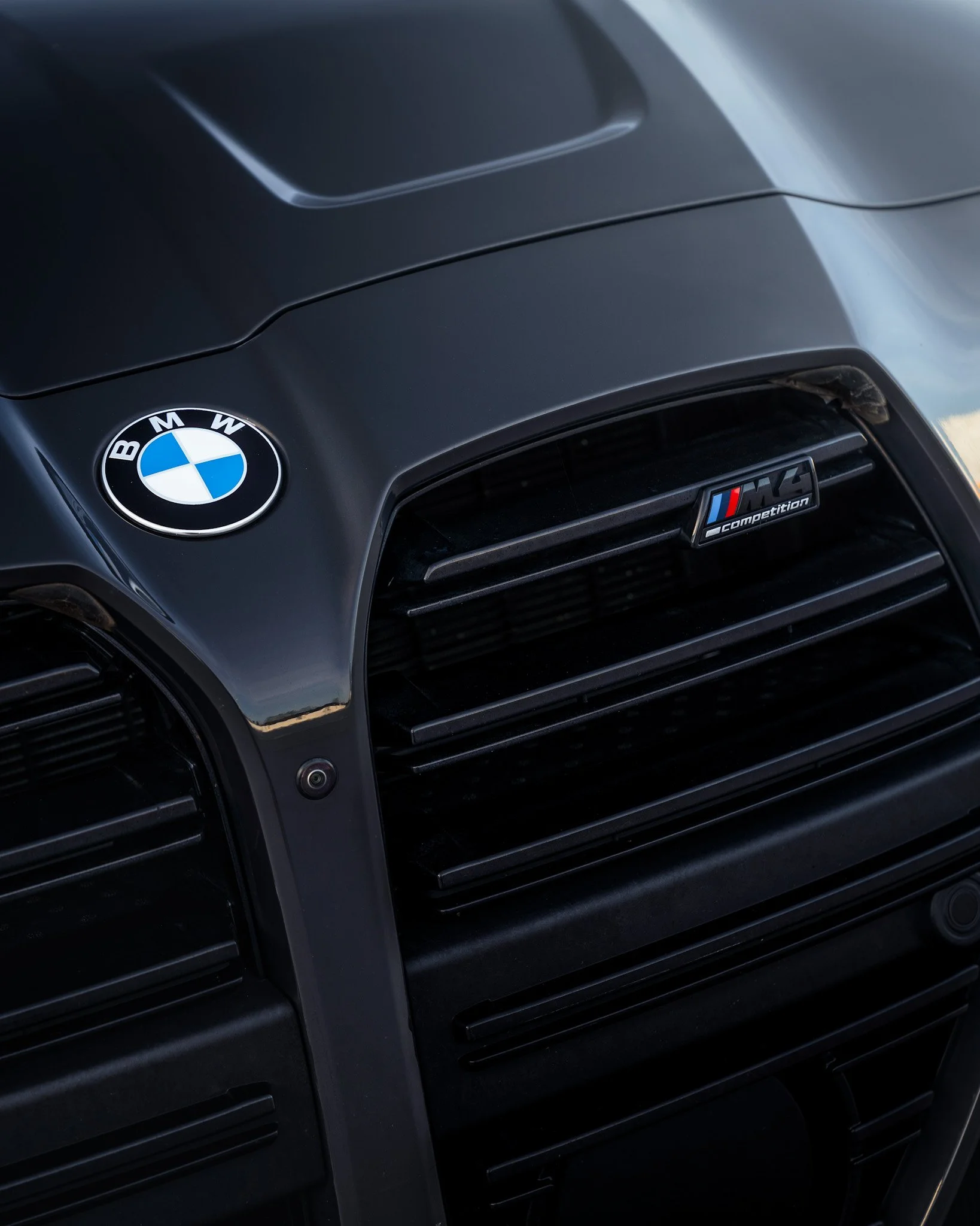 Close-up of the front grille of a black BMW car with BMW and M Competition badges.