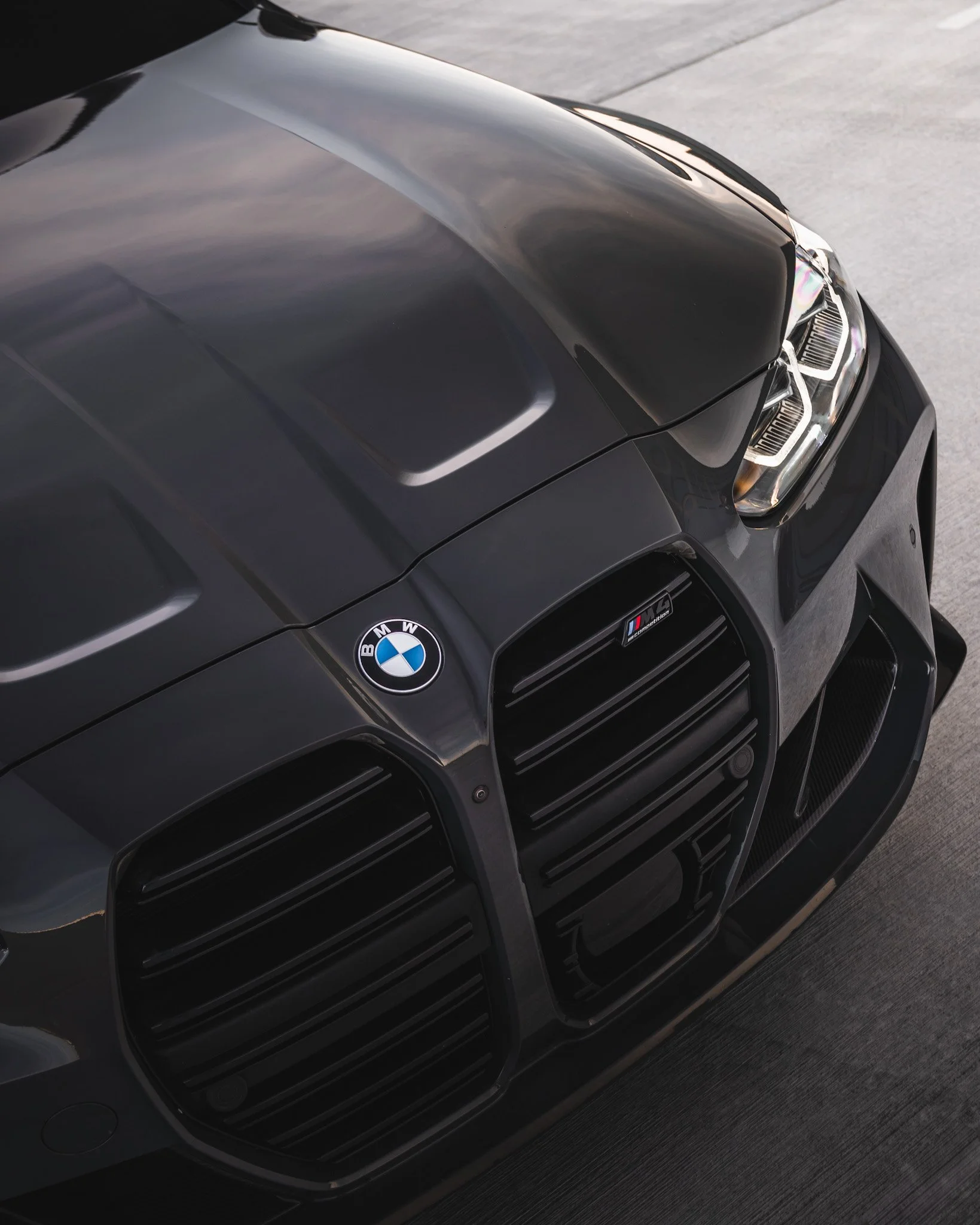 Front view of a black BMW M vehicle with BMW and M logos, showing the hood, grille, and headlights.