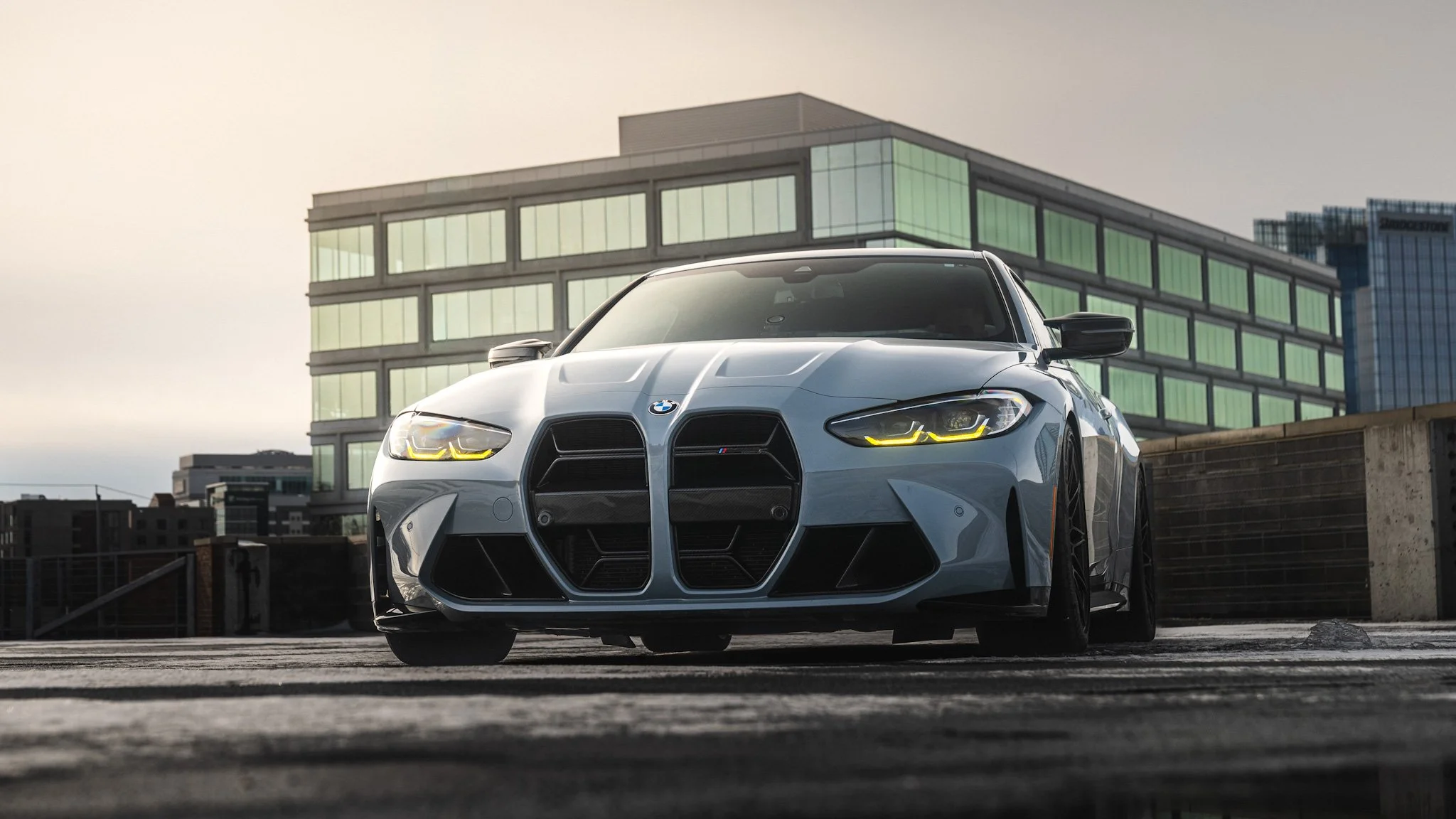 A white BMW sports car parked on a rooftop parking lot with modern glass buildings in the background during daytime.