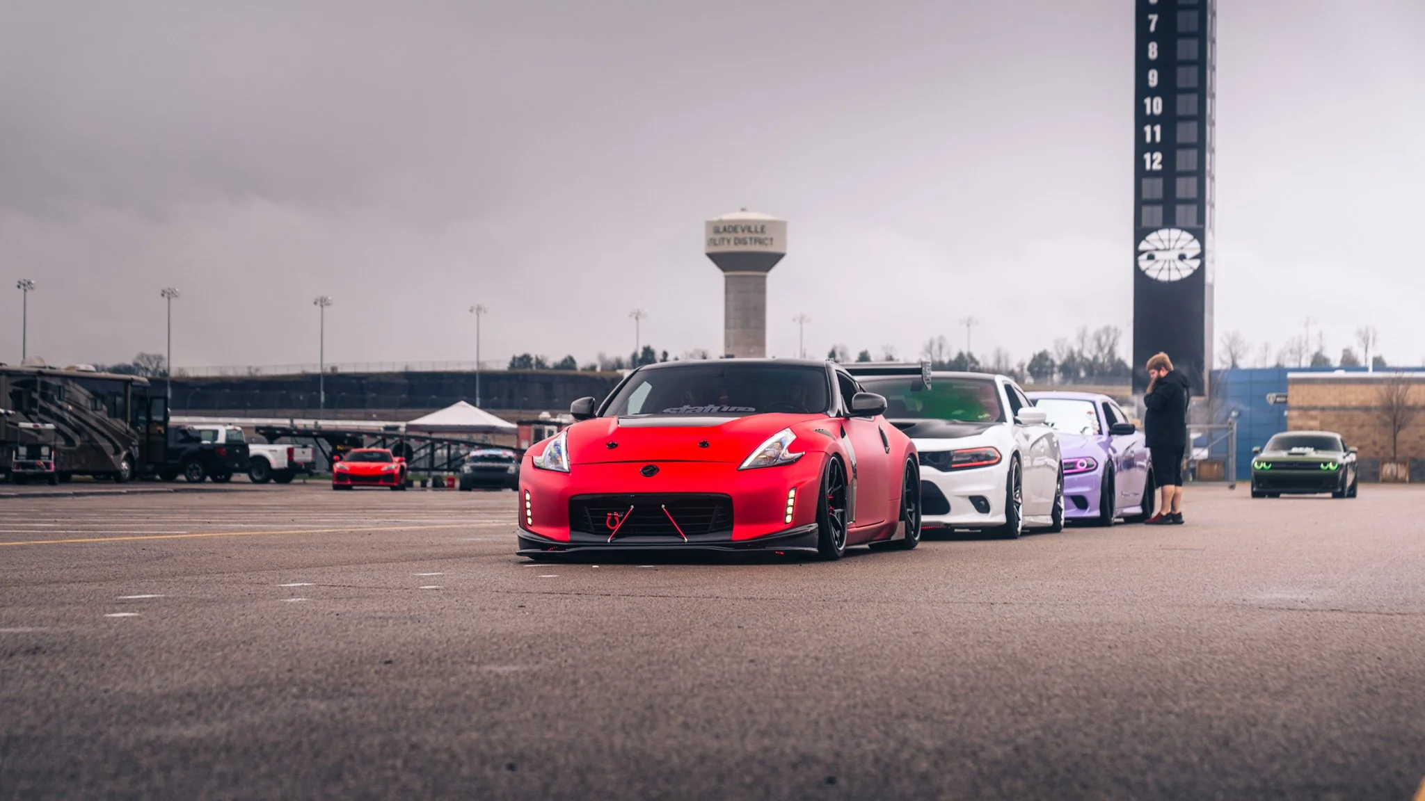 Lineup of red Nissan 370z, White Dodge Charger, Purple Dodge Charger, with a challenger in the back creeping up all at stoopicold at the nashville super speedway