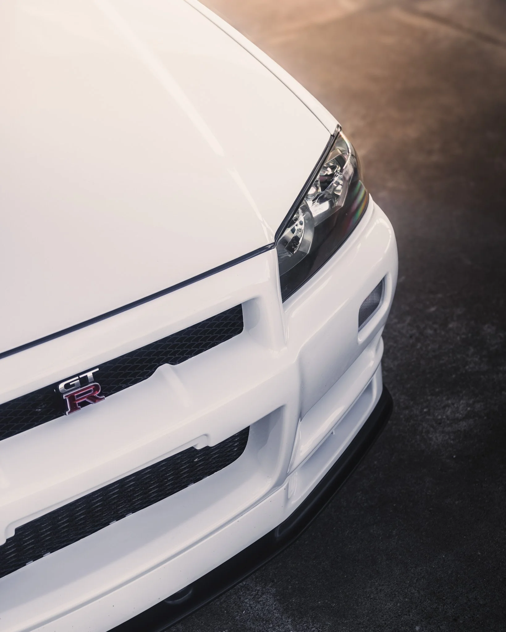 Close-up of the front right corner of a white Nissan GT-R sports car, showing the headlight, grille, and bumper.