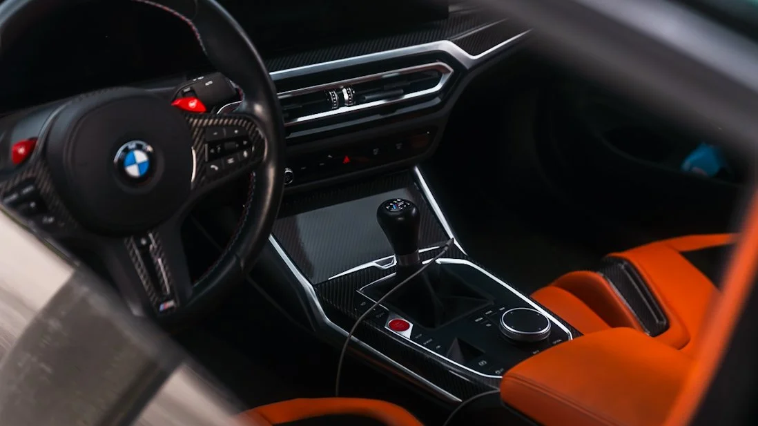 interior shot 2 of green BMW m4 showcasing the orange interior, shifter, and steering wheeel
