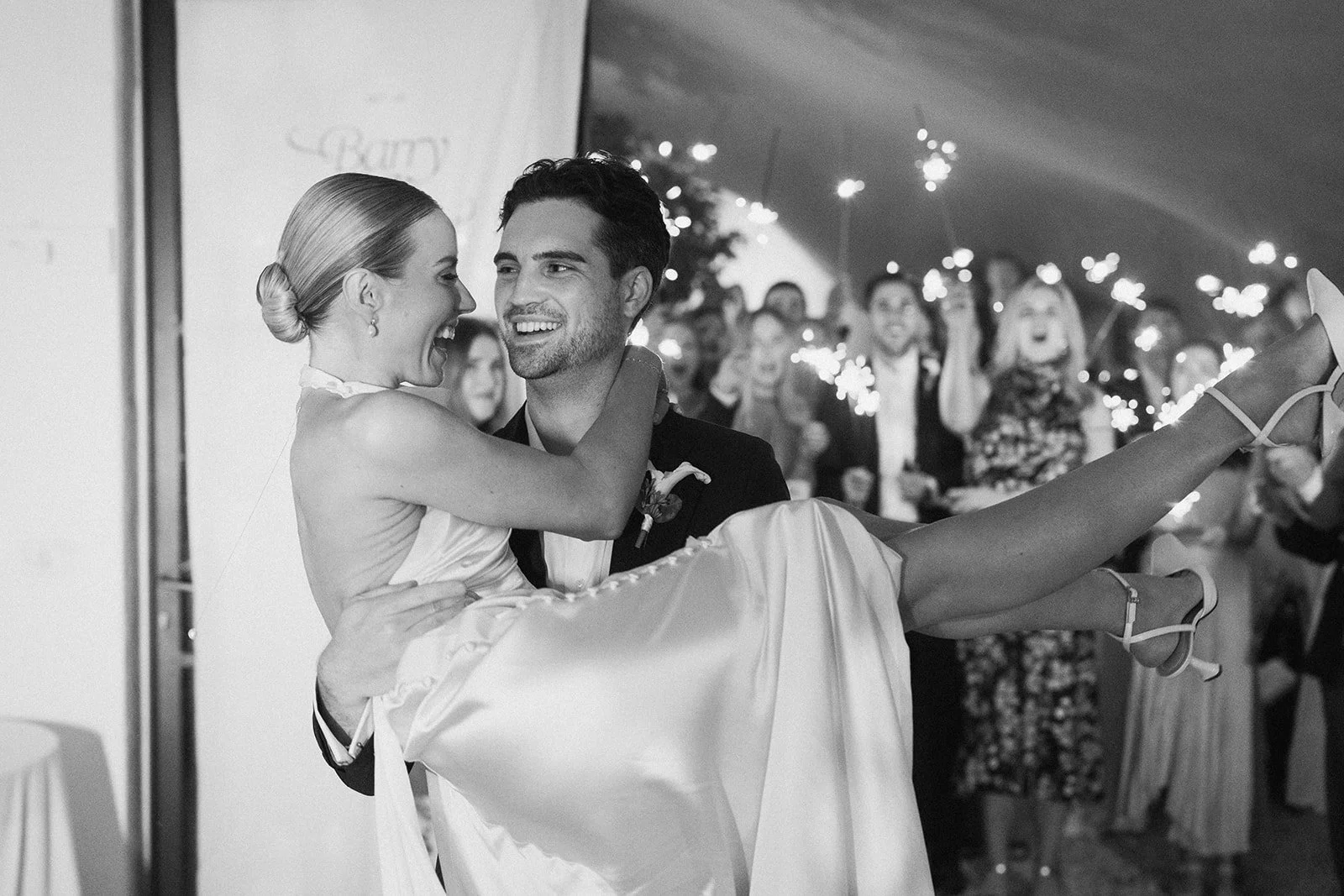 A happy wedding couple smiling, with the groom holding the bride in his arms.