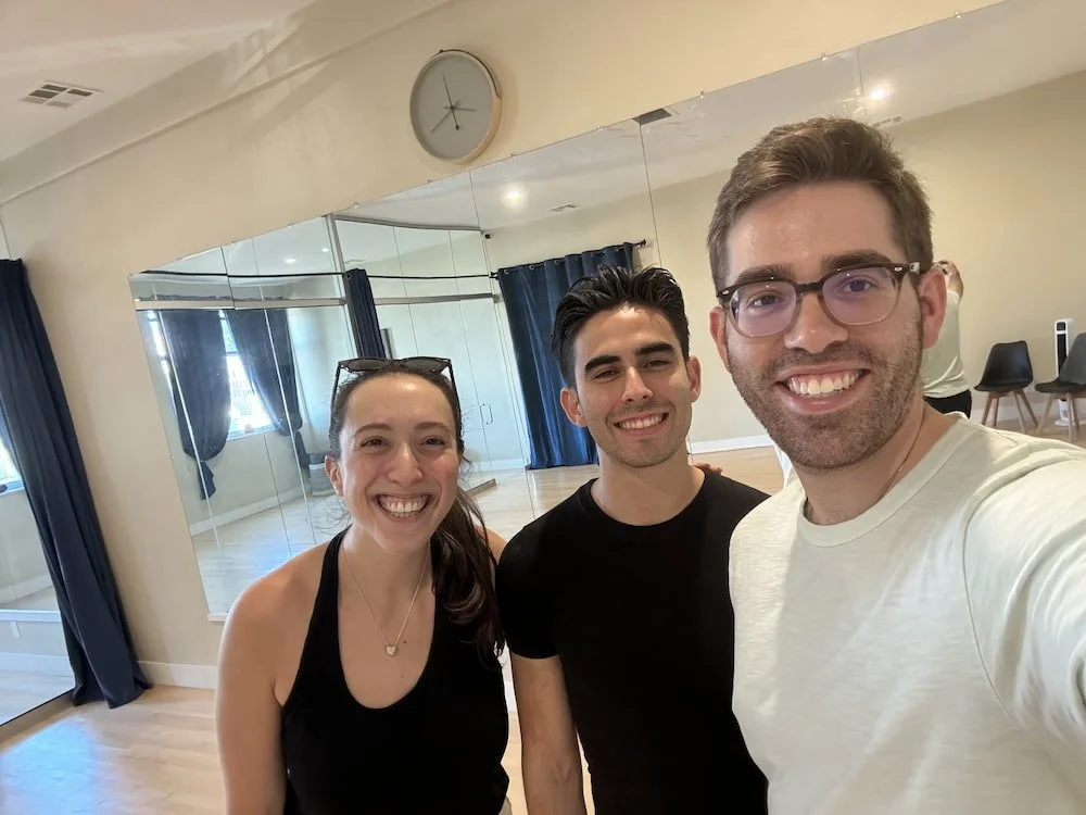 Richard, a San Francisco-based wedding dance instructor, smiling and taking a selfie in a dance studio with one of his wedding dance couples.
