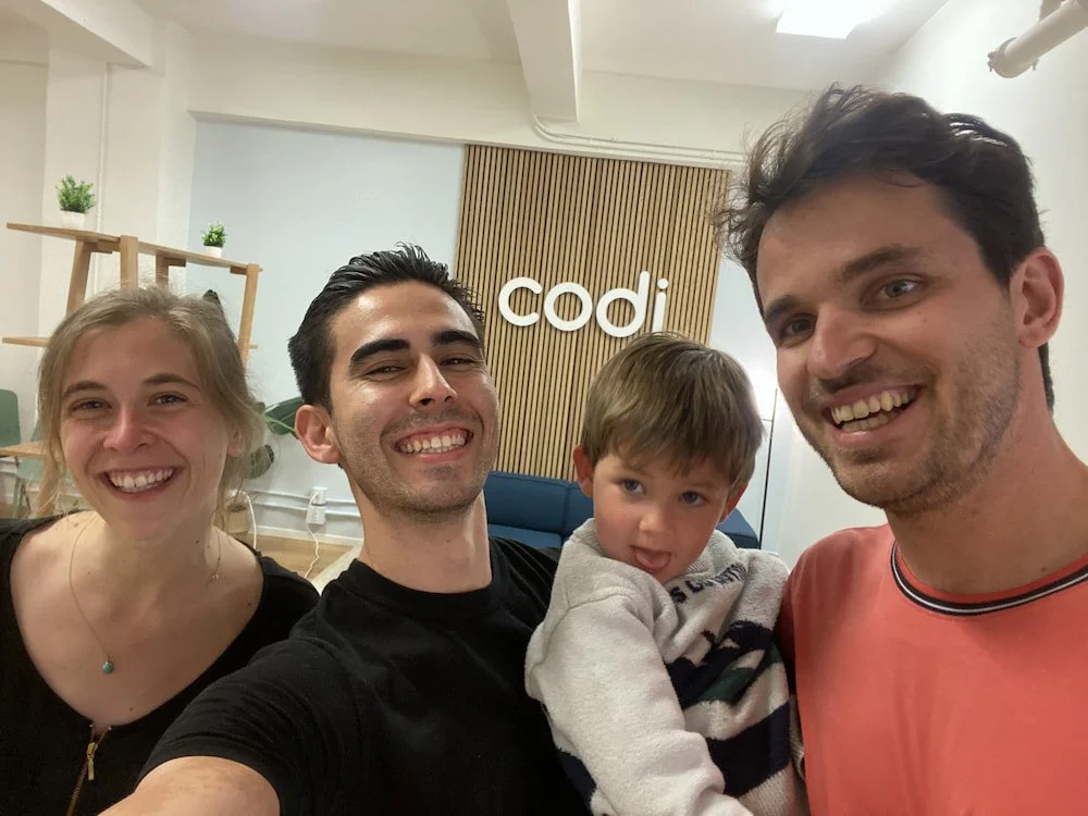 Richard, a San Francisco-based wedding dance instructor, smiling and taking a selfie in a dance studio with one of his wedding dance couples and their young child.