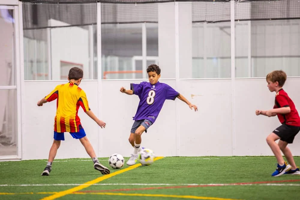 Three boys playing soccer in an indoor soccer field.