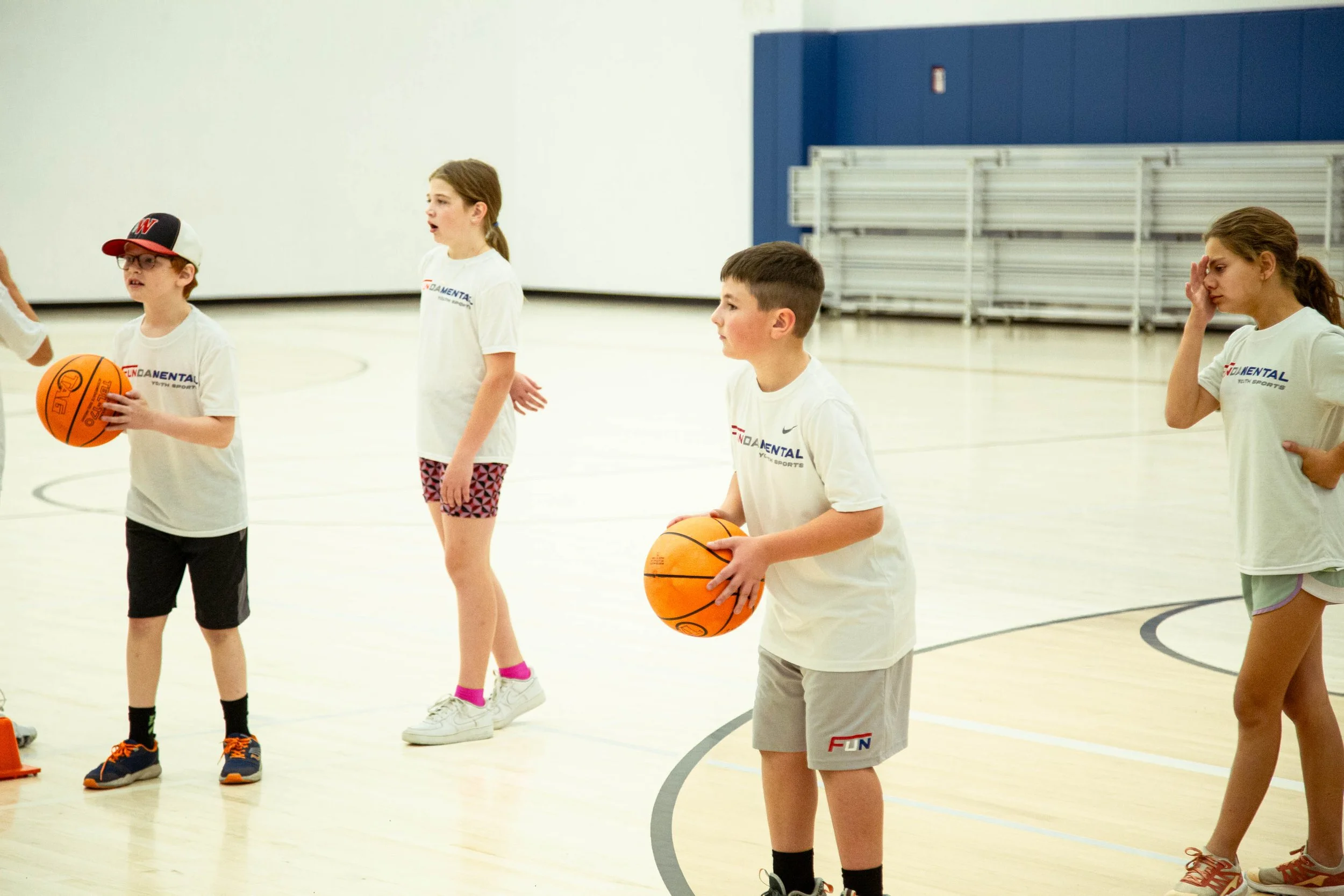 Children practicing basketball in a gym, holding basketballs on the court.