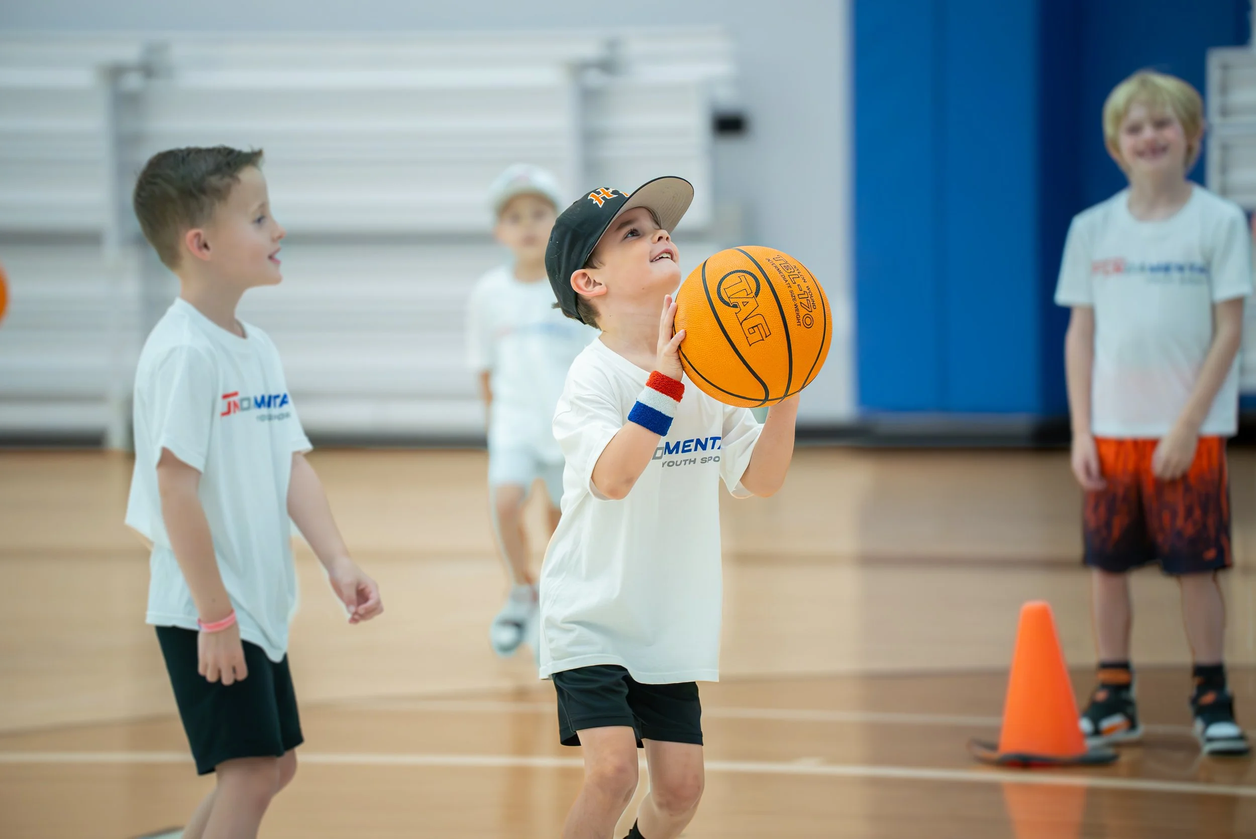 Children playing basketball indoors, with one boy preparing to shoot the ball while others watch.