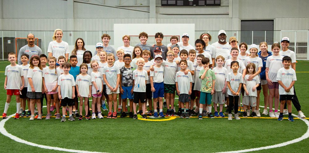 A large group of children and adults posing for a photo on an indoor sports field.