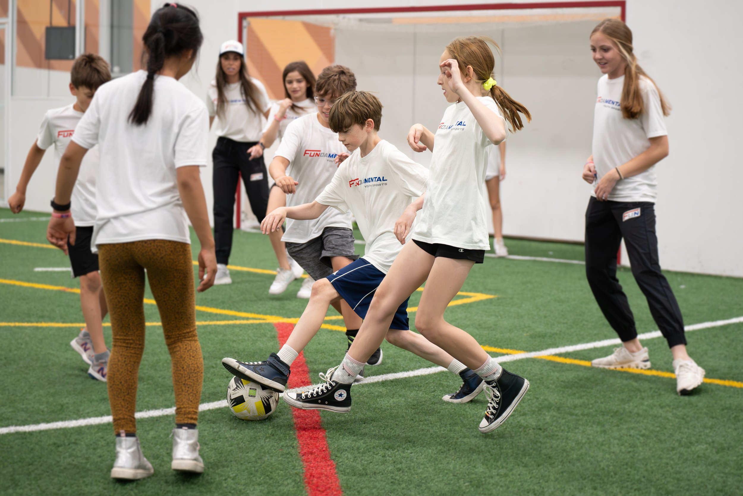 Children playing indoor soccer or football on a green turf field.