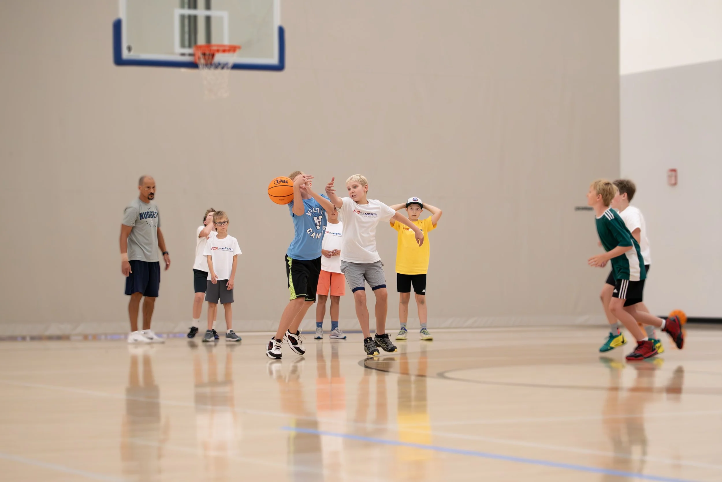 Children and a coach playing basketball in an indoor gym.