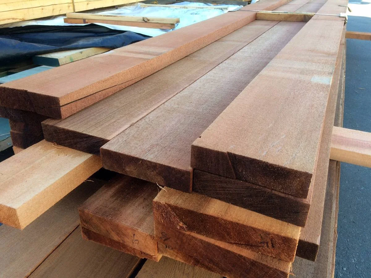 Several pieces of lumber, mainly pinkish and brown in color, stacked on a workbench in a building or construction site.