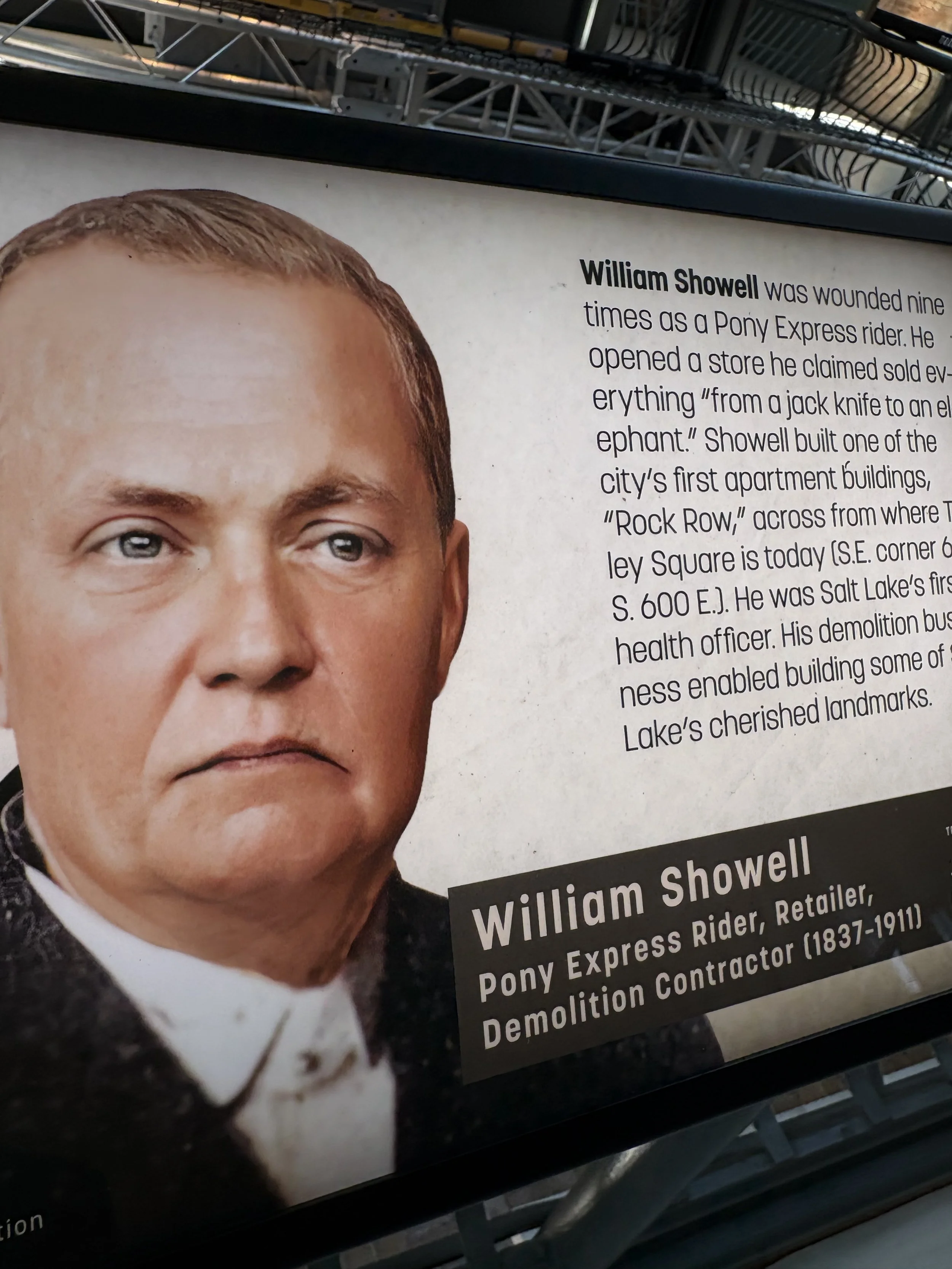 Portrait of William Showell, a man with short light brown hair and blue eyes, dressed in a suit with a bow tie, with a background of text about him.