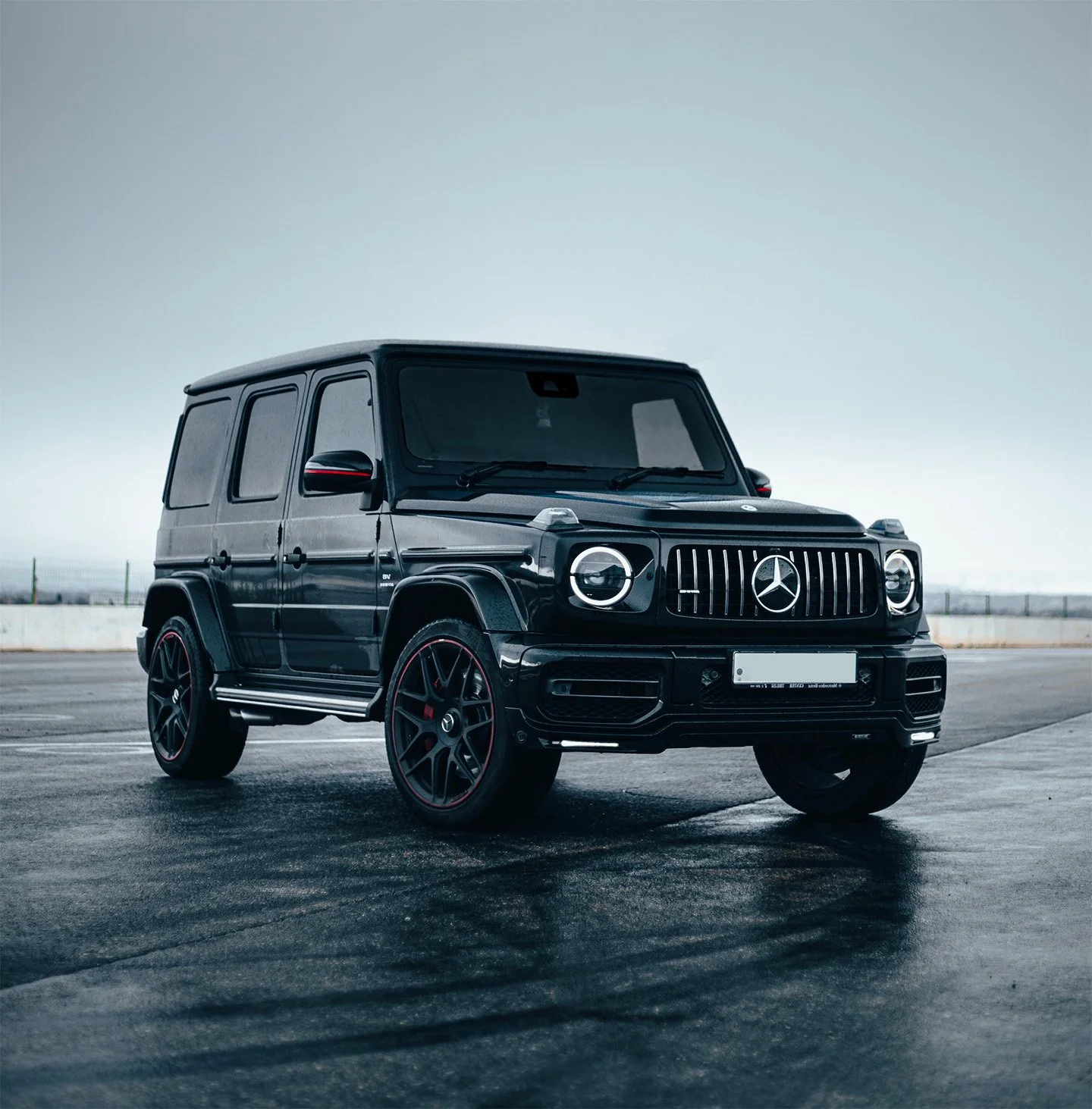 A black Mercedes-Benz G-Class SUV parked on an empty paved surface under a cloudy sky.
