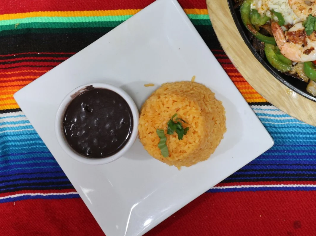 A plate with a serving of Mexican rice and a bowl of black beans, placed on a colorful, striped tablecloth.