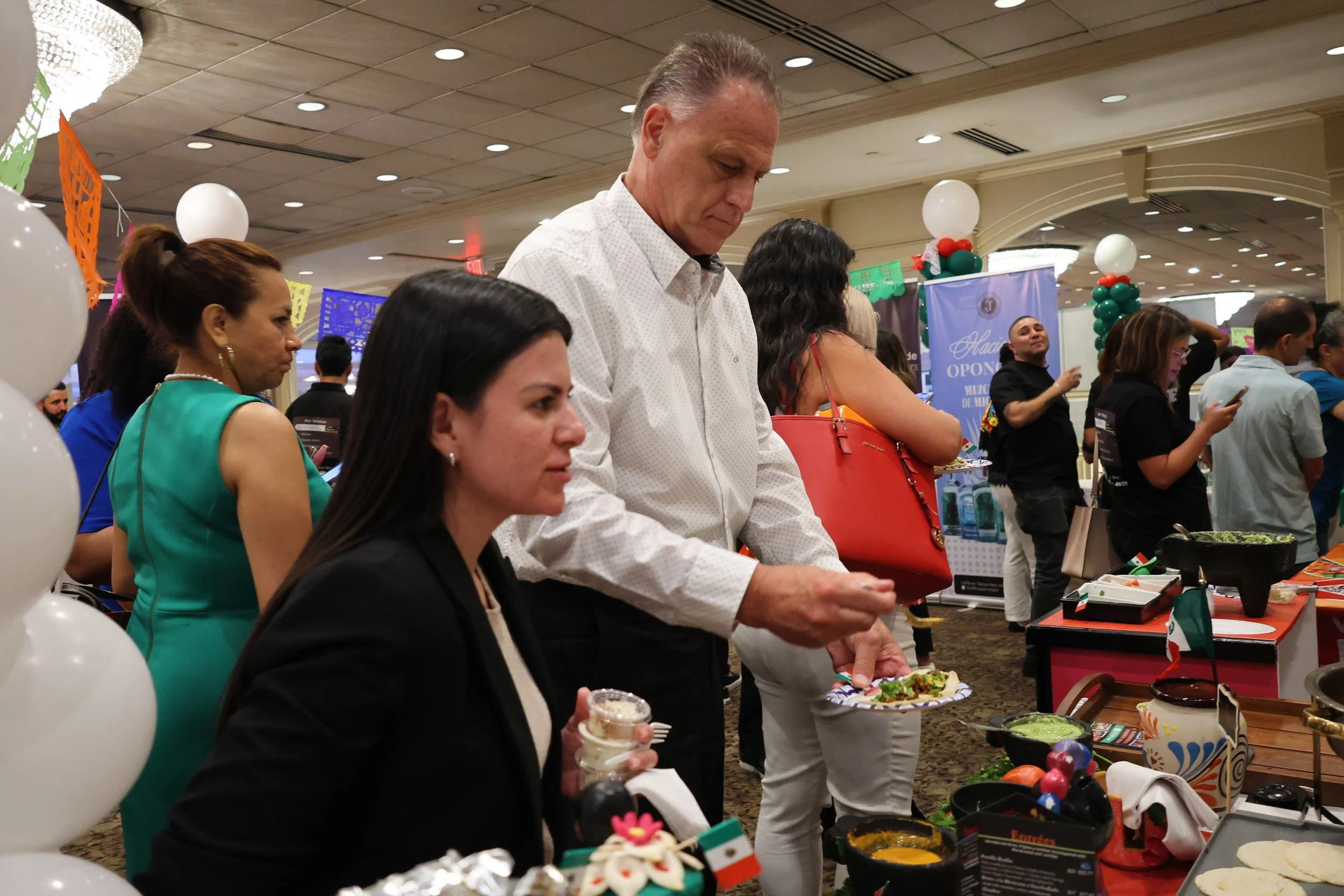 People attending a cultural event, with Mexican decorations and food display.