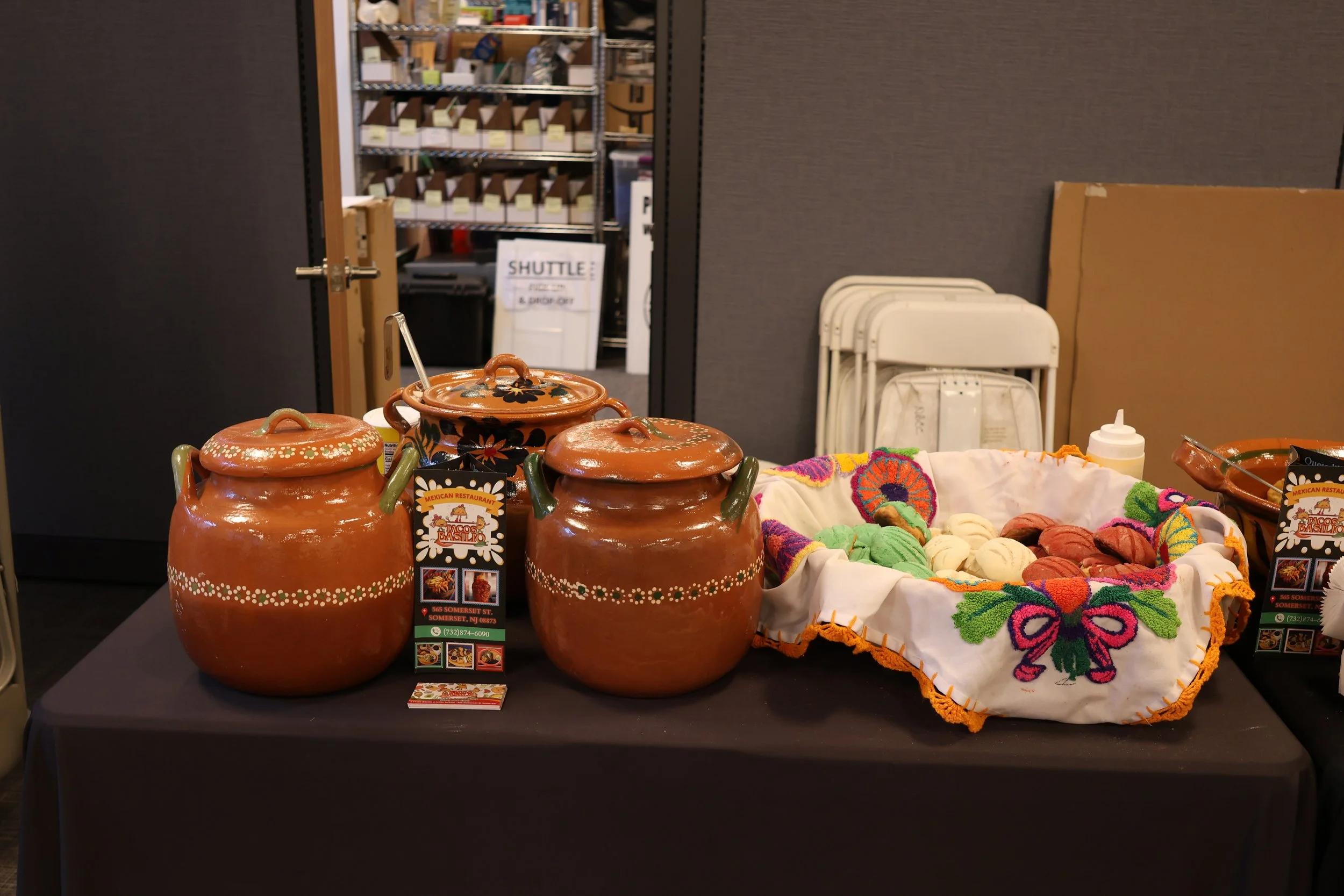 Display of traditional Mexican clay pots, colorful embroidered textiles, and a tray of assorted cookies at a market or fair.