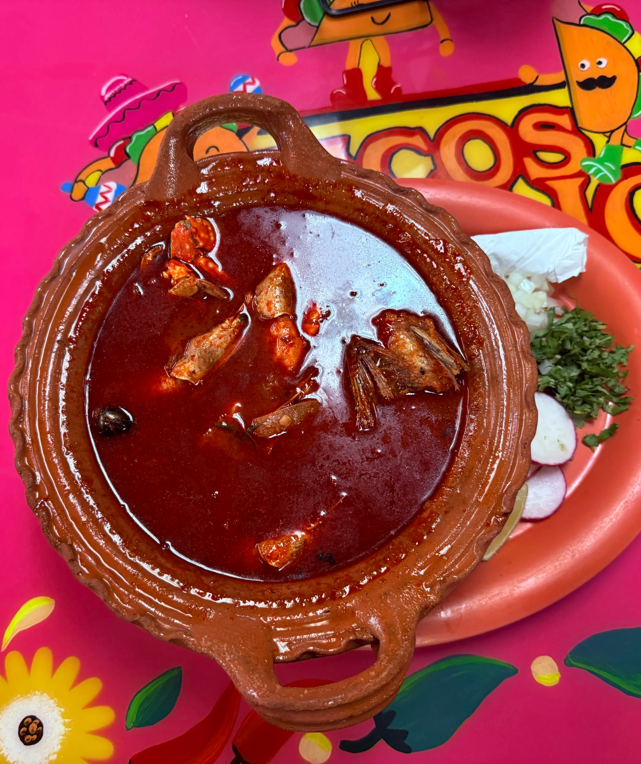 A taco-shaped container filled with red sauce and seafood, placed on a colorful tray with cartoon characters and flowers.