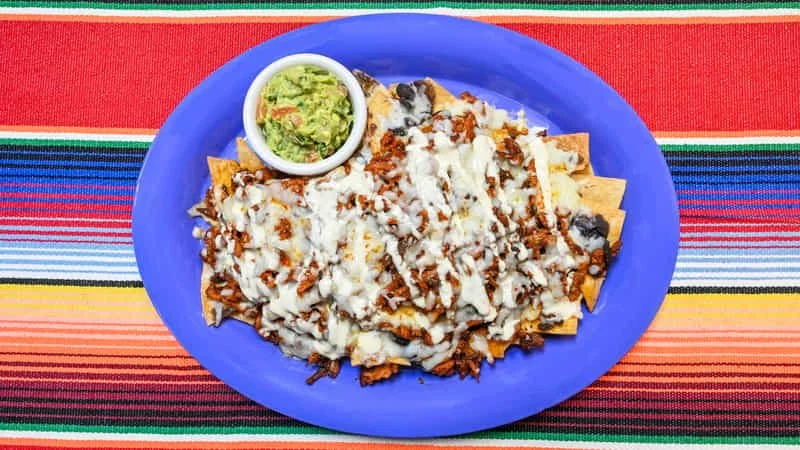 Plate of nachos topped with melted cheese, with a side of guacamole on a colorful striped tablecloth.
